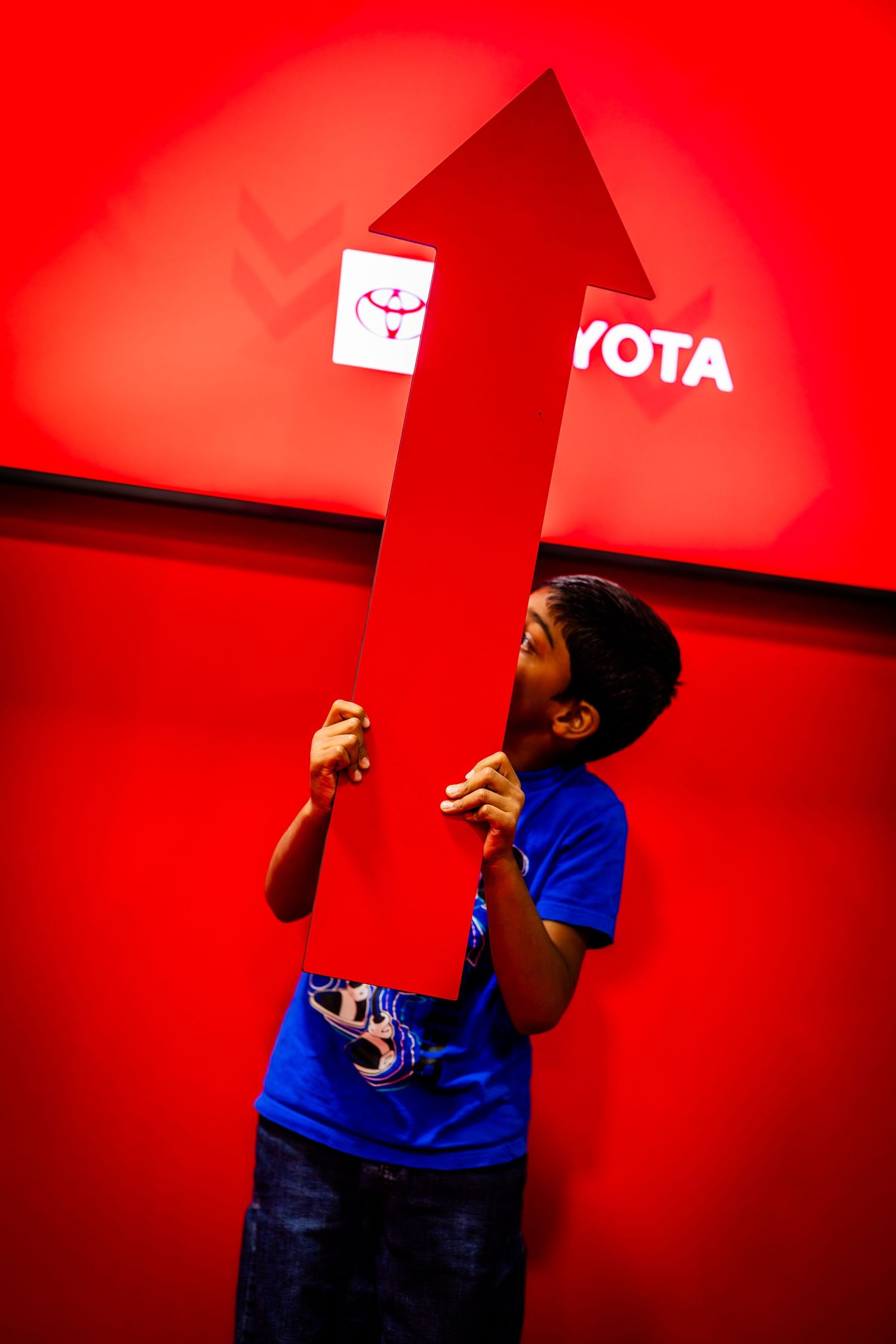 Person in blue shirt against vibrant red wall making expressive gestures.