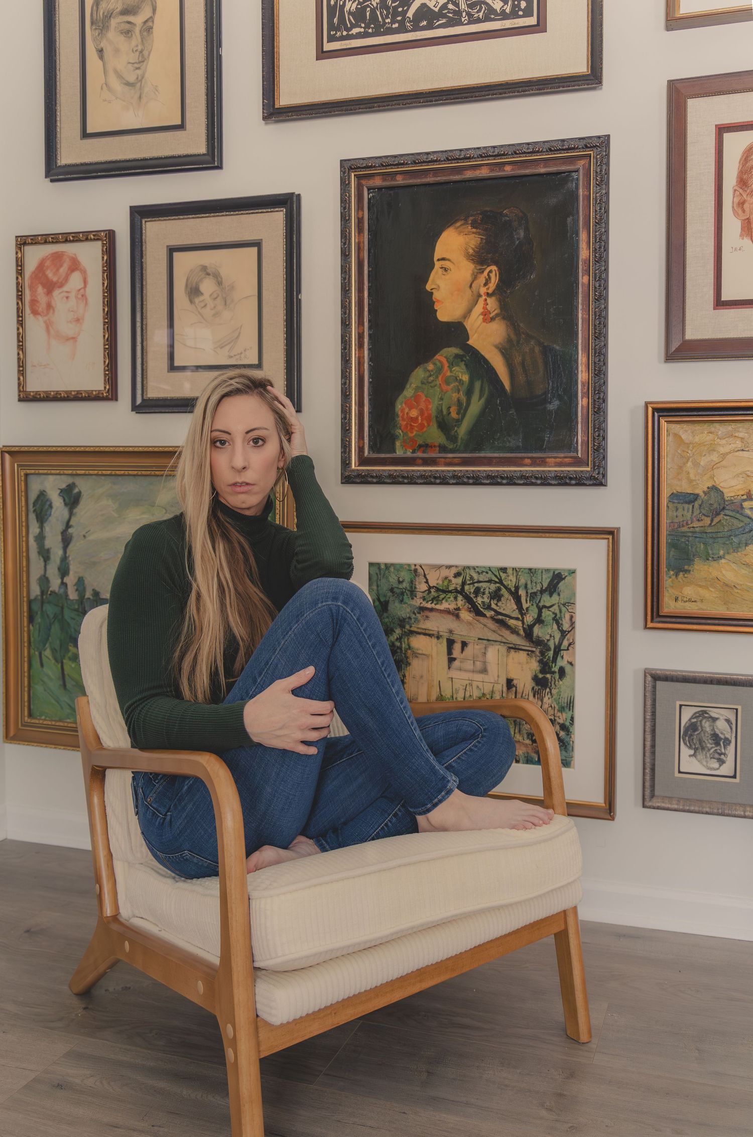 Gallery wall features artwork and portraits while someone in blue sits on a modern wooden daybed with white cushions.