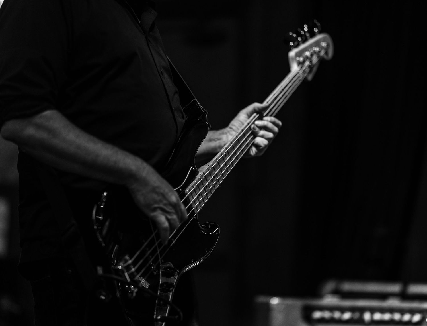Close-up black and white shot of hands playing bass guitar.