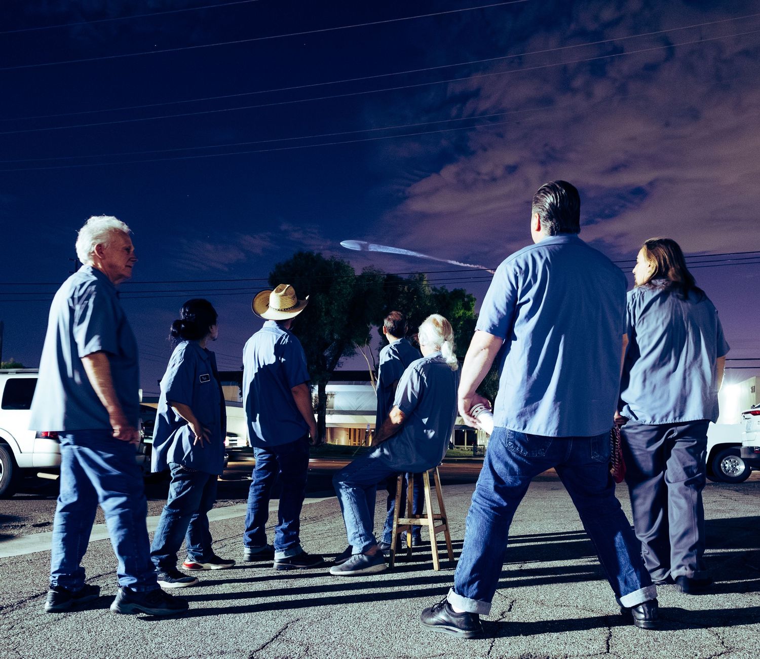 People in blue clothing arranged in casual formation outdoors during twilight hours.
