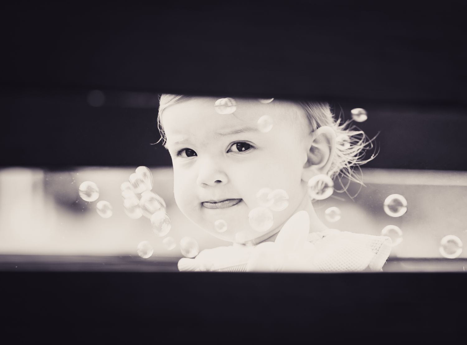 Black and white photo of a cute toddler smiling surrounded by floating soap bubbles.