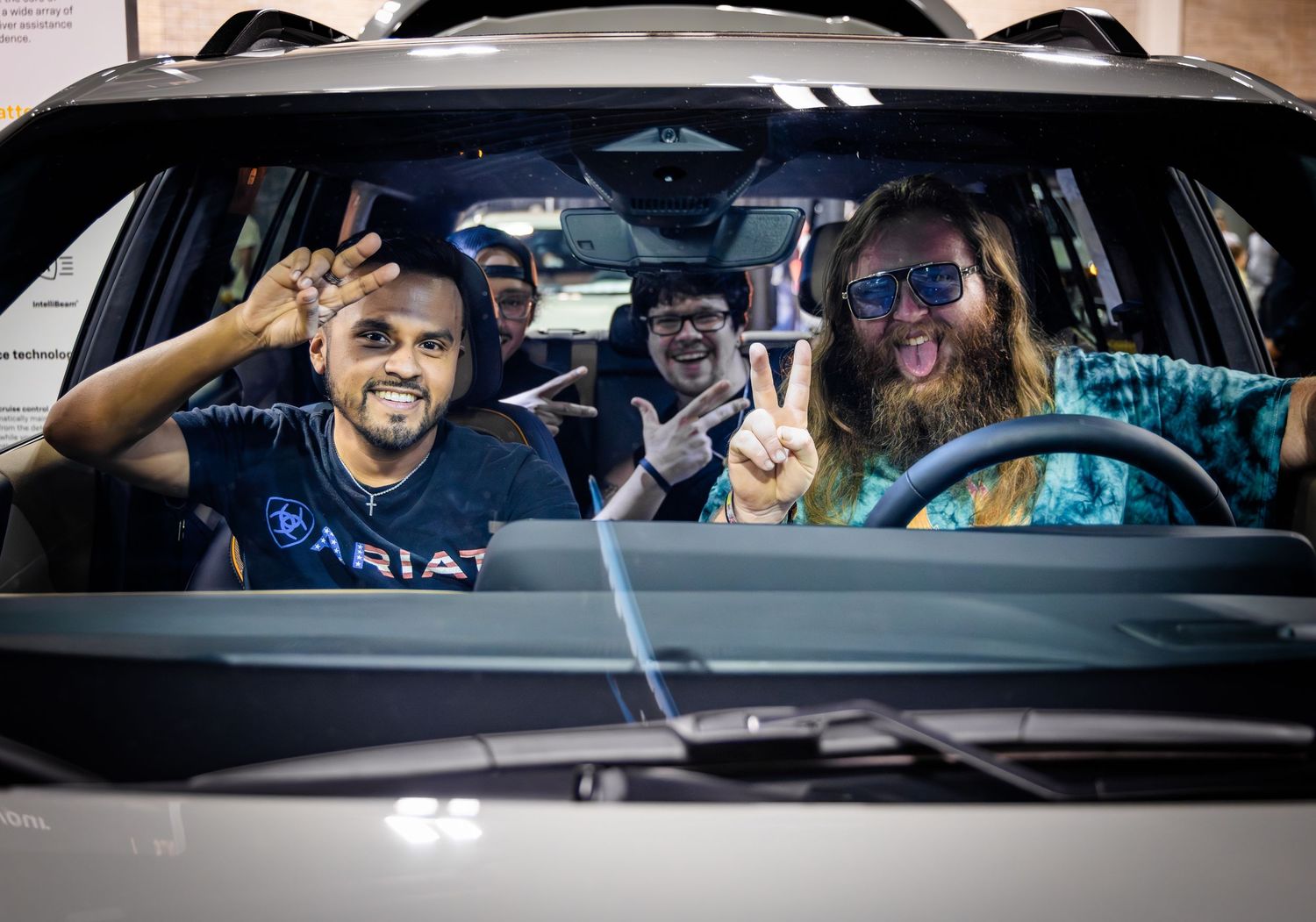 Three friends in a car making silly faces and peace signs through the windshield while wearing sunglasses.
