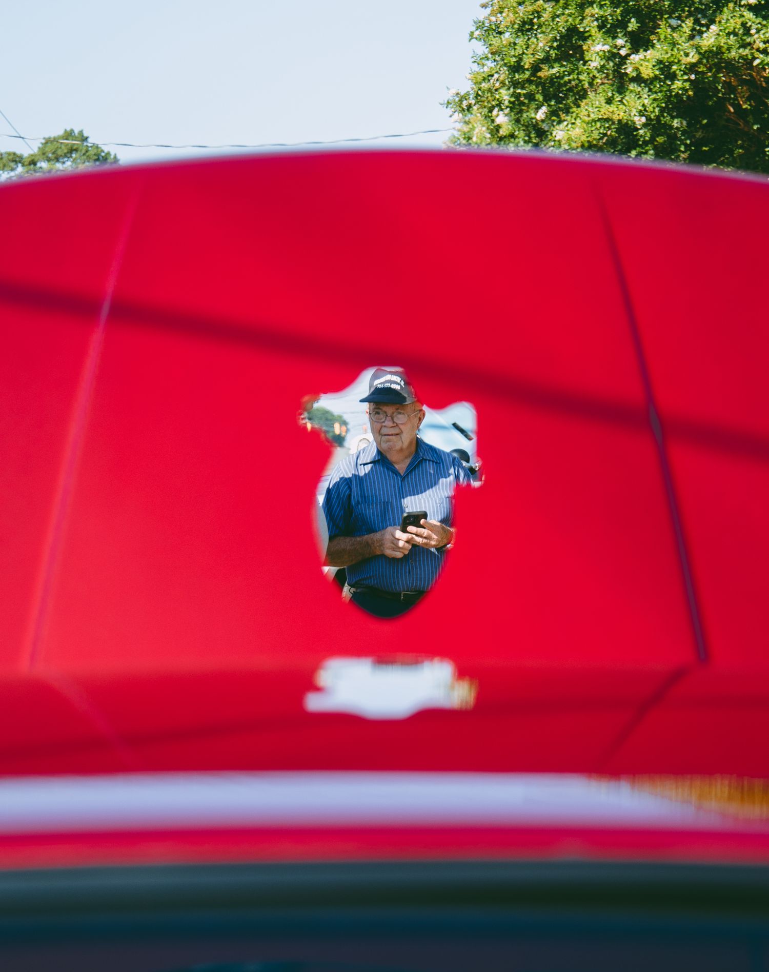 Red car hood reflecting sky and trees in its glossy paint finish.