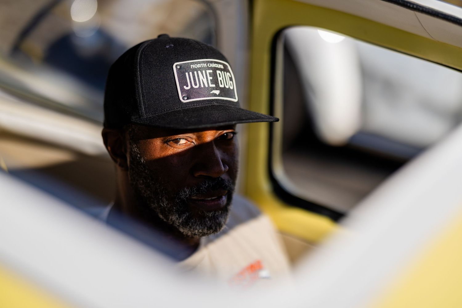 Man wearing black June Bug cap and face mask sitting inside a yellow vehicle.