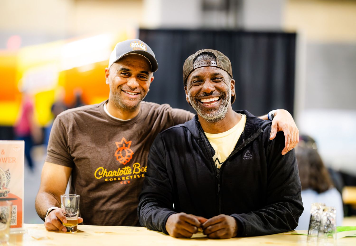 Two friends share a laugh while enjoying drinks at an outdoor event.