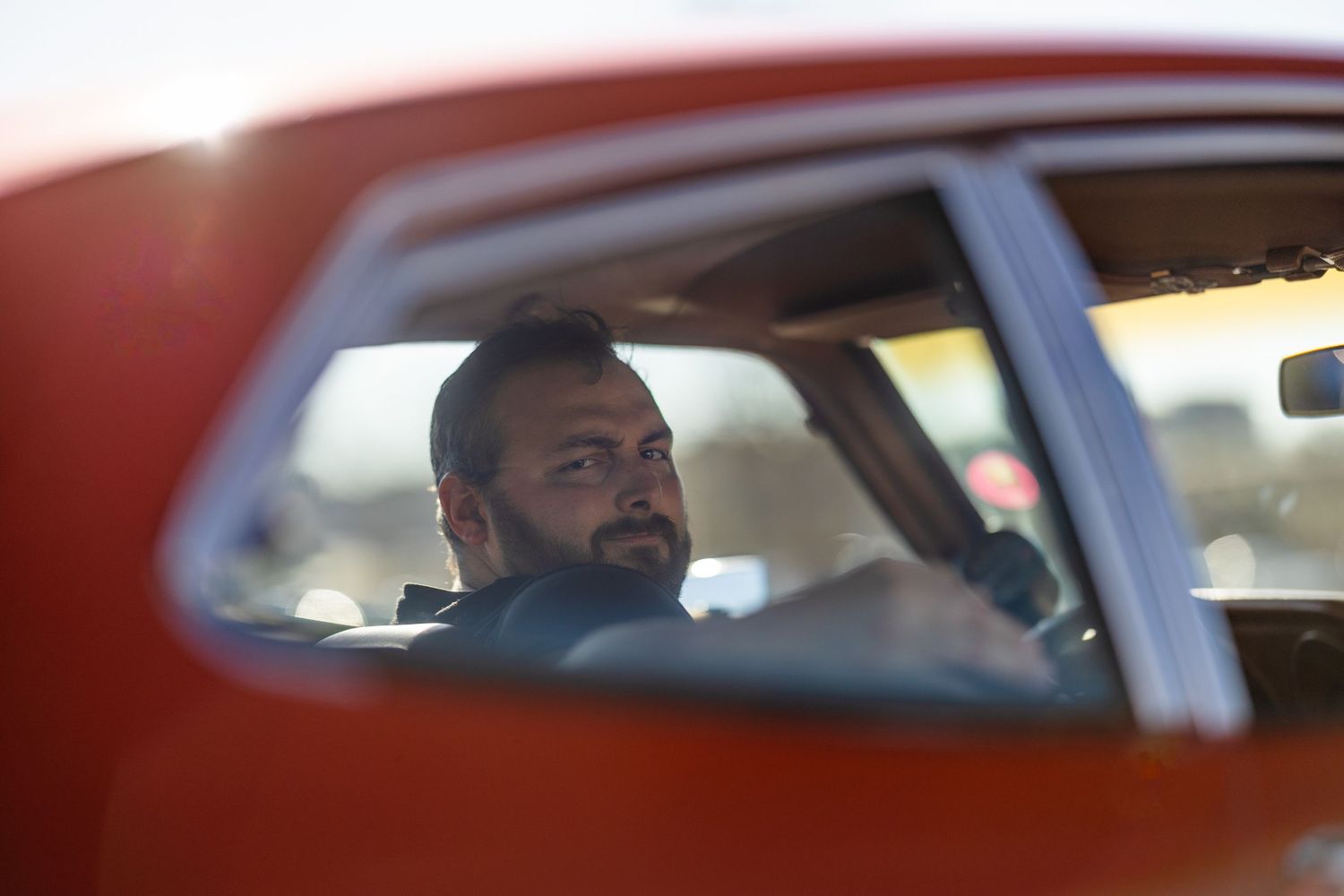 View through car window showing someone sitting in driver's seat during sunset.