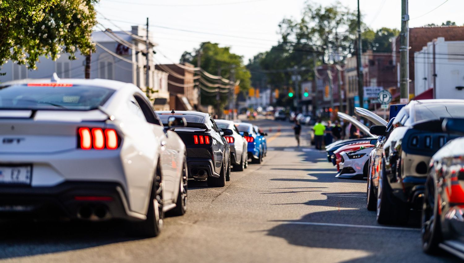 A row of Ford Mustang cars parked along a sunny urban street during a car show event.