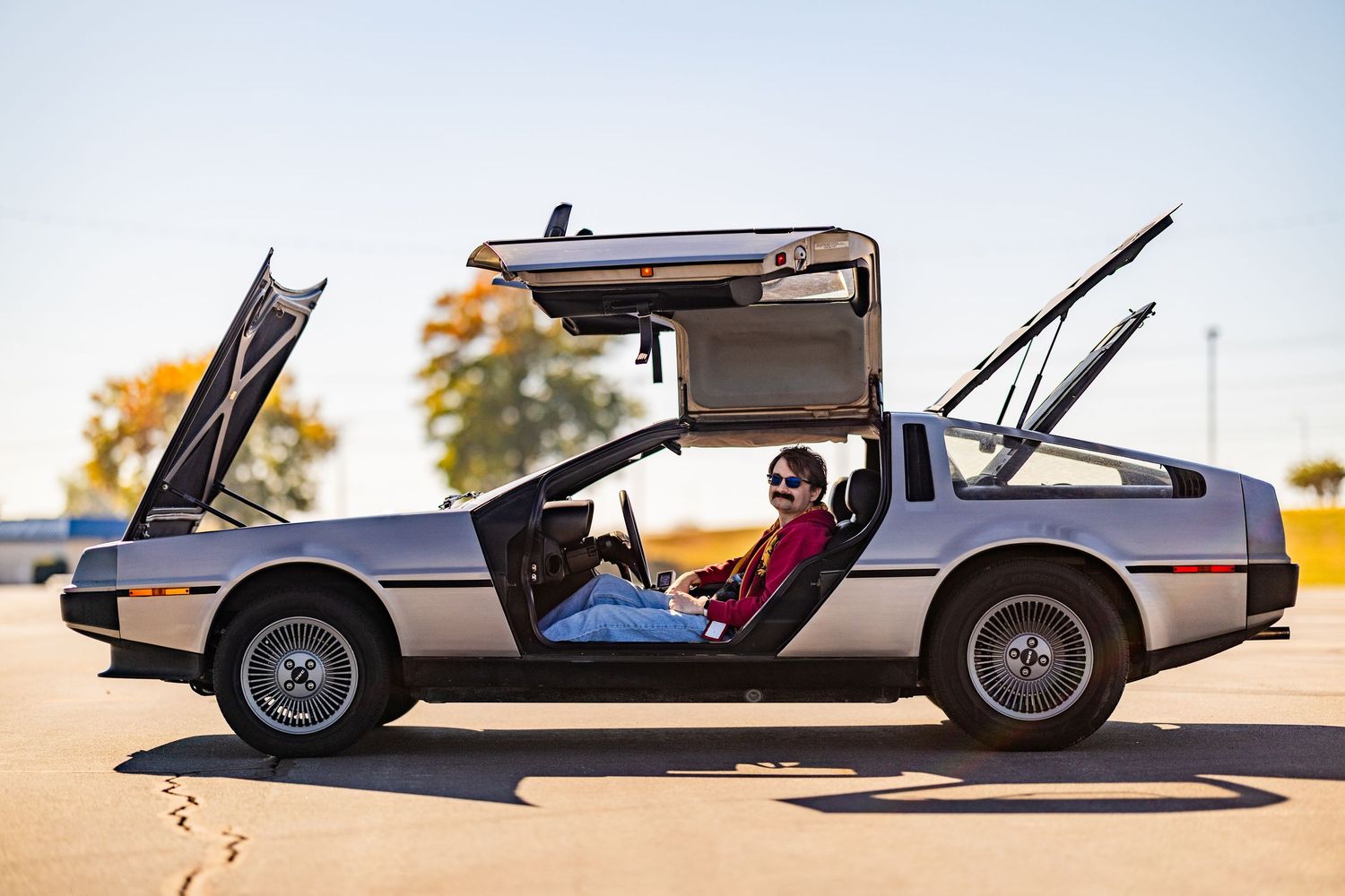 A silver DeLorean car with its distinctive gull-wing doors open on display at a car show.