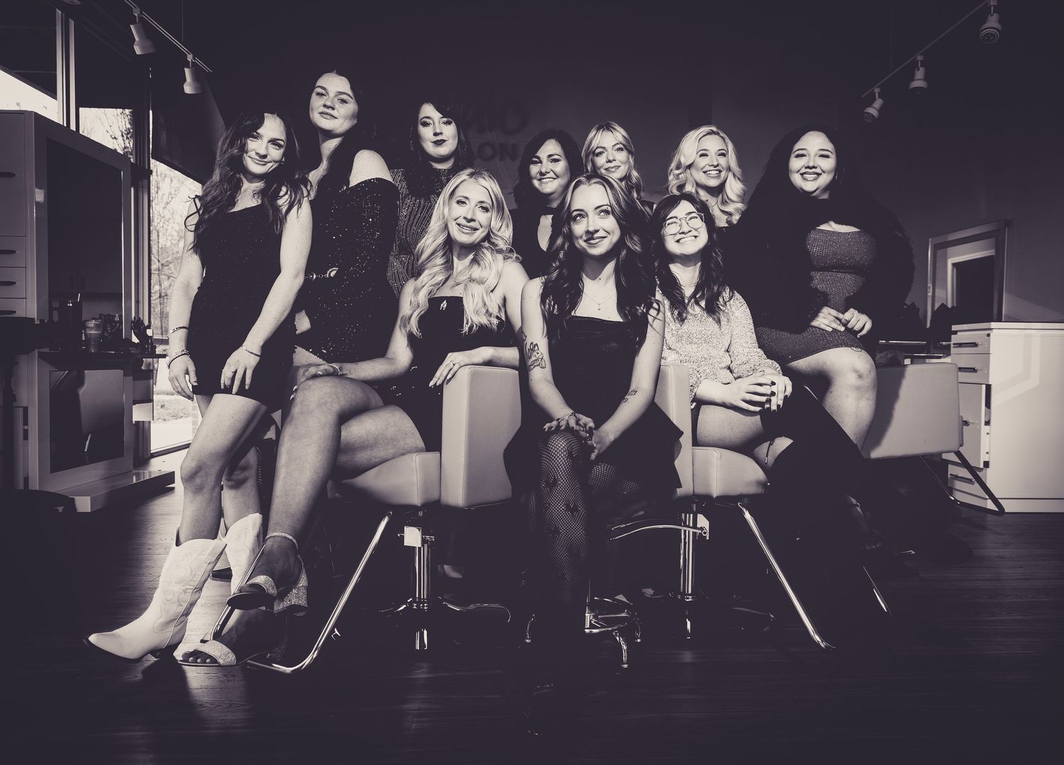 A group portrait of friends in black dresses seated on bar stools in a studio setting.