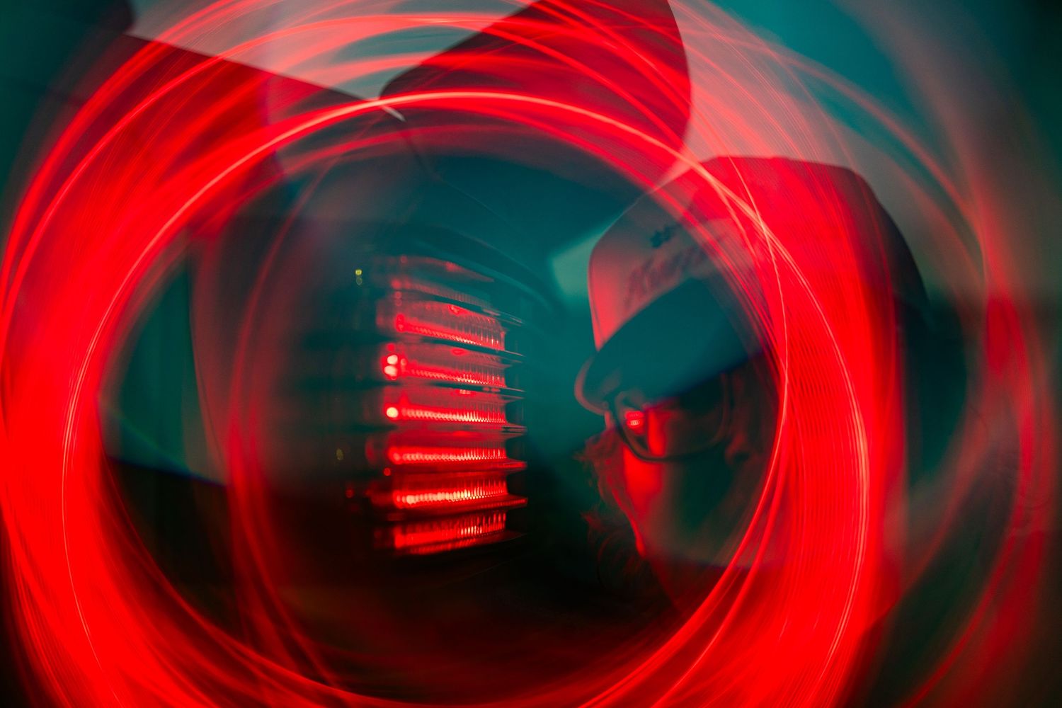 Abstract long exposure photo with swirling red light trails surrounding a silhouetted figure in darkness.