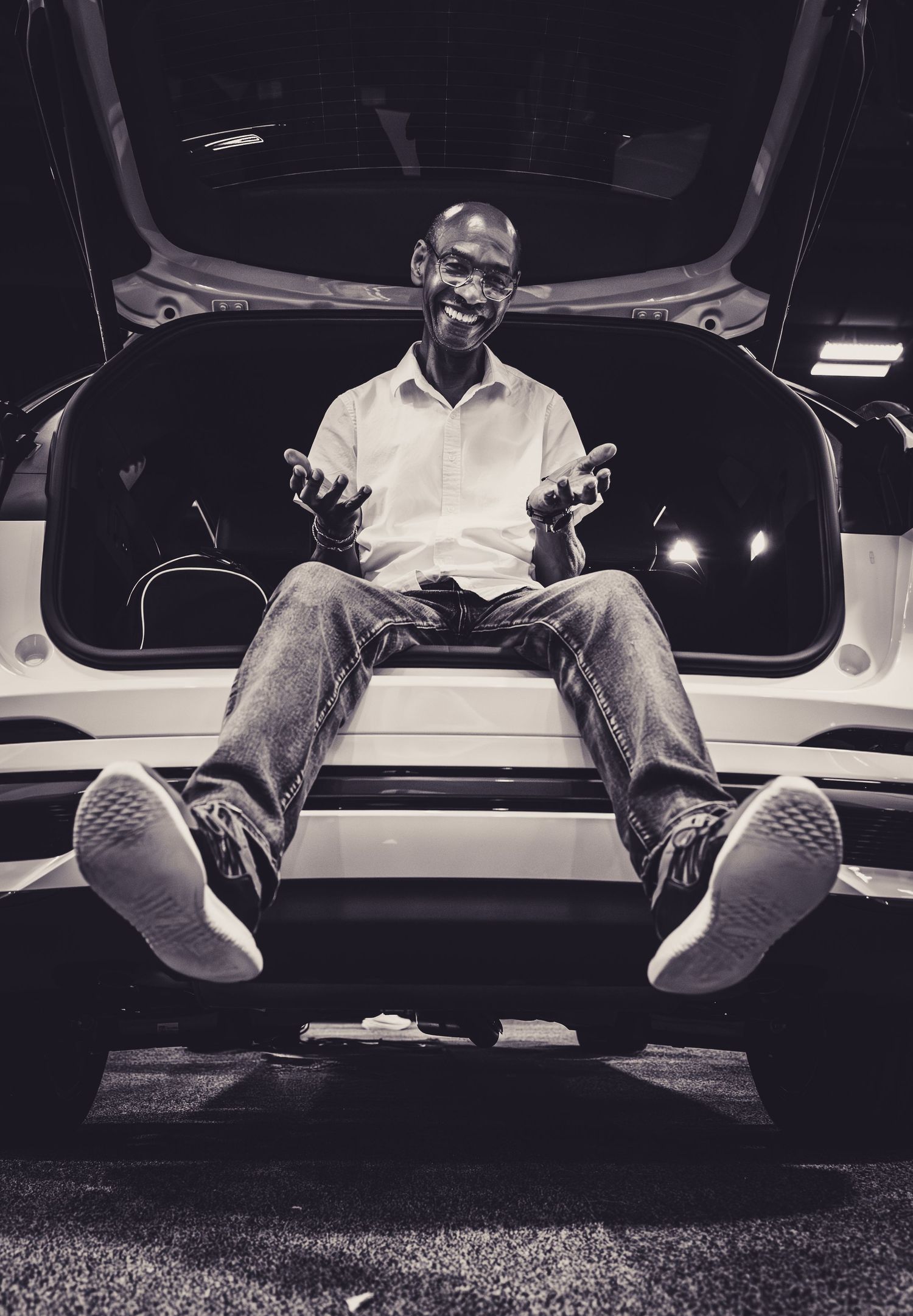 Black and white photo of someone sitting in a car trunk at night.