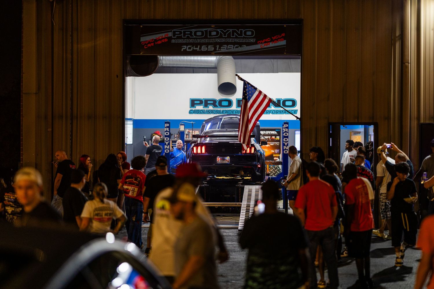 Crowd gathers at Pro Uno automotive event entrance with American flag displayed on dark car under dramatic lighting.