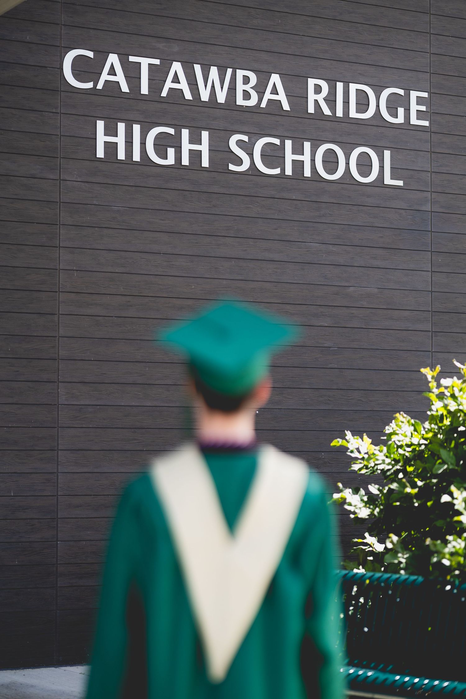 Graduate in green cap and gown stands before Catawba Ridge High School sign on graduation day.