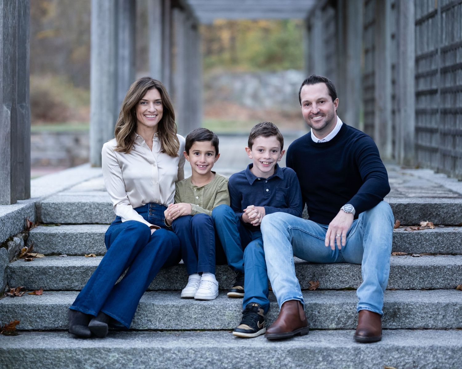 Family wearing blue jeans sitting together in a series of outdoor stone steps during an autumn photoshoot.