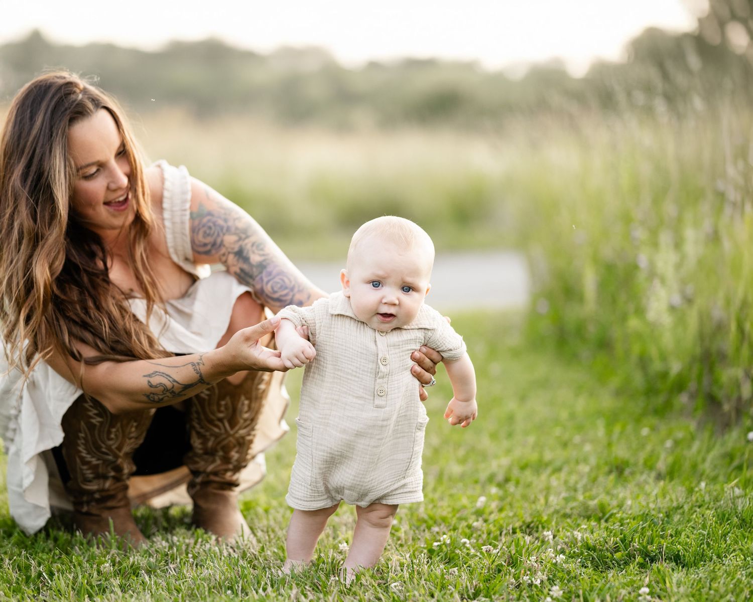 Mother helps baby take first steps in lush green grass on a sunny summer day.
