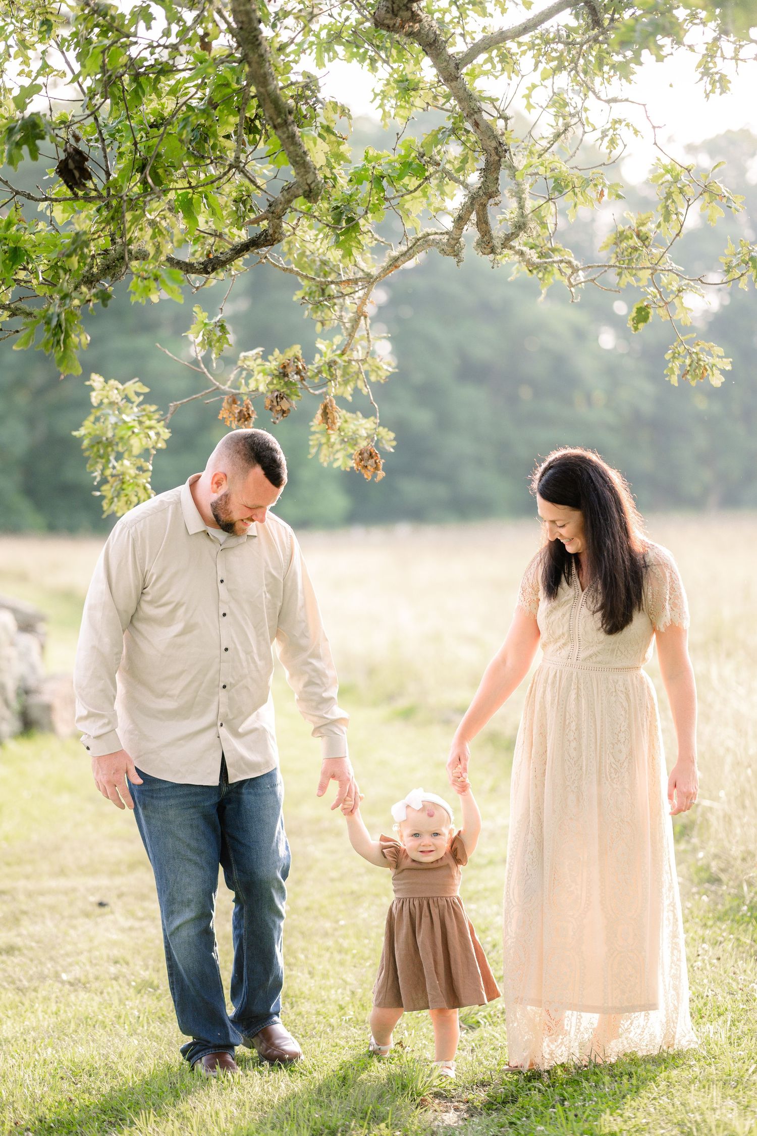 A tender family moment under blooming tree branches in a sunny meadow during golden hour.