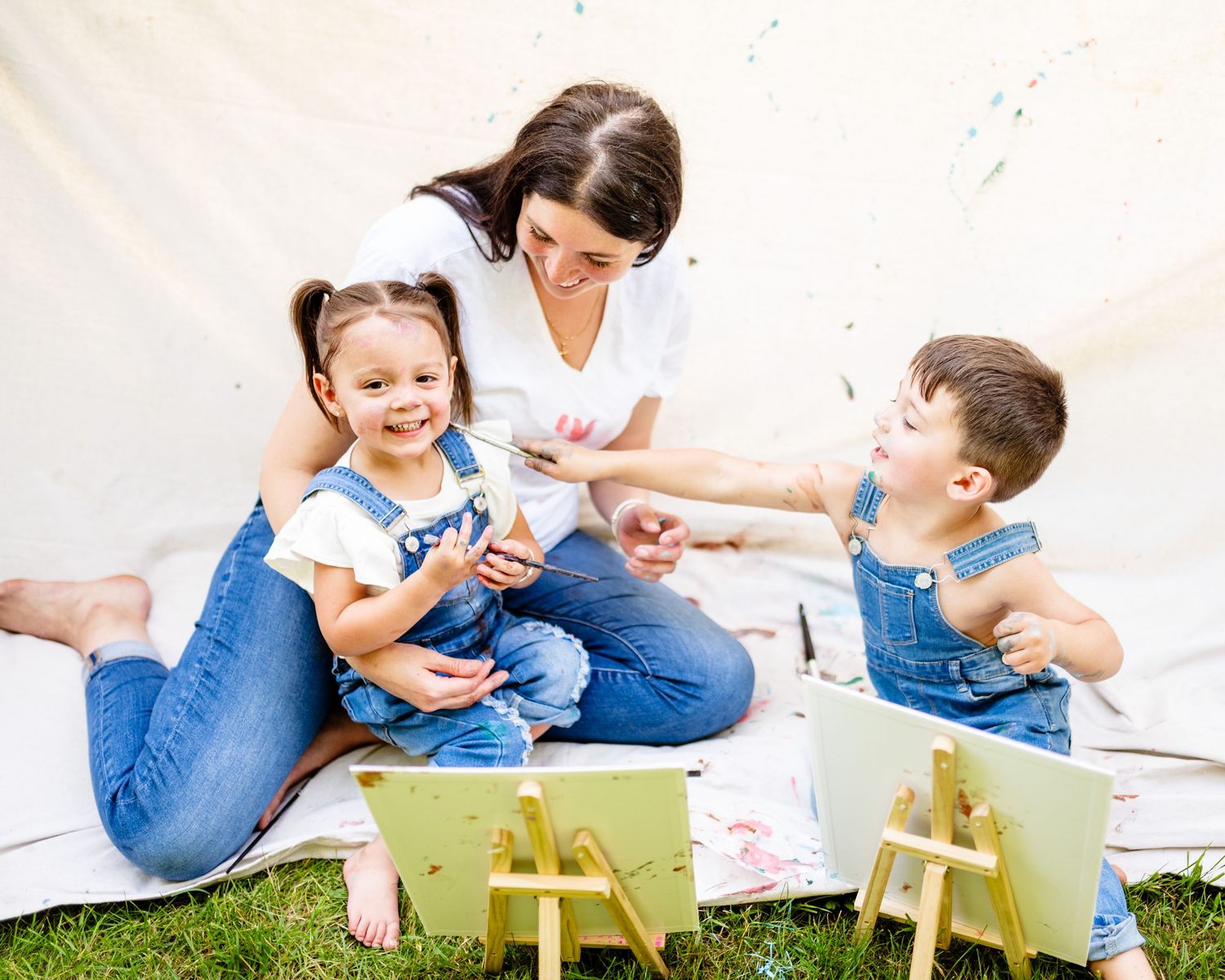 Family sitting together on grass enjoying picnic lunch with small wooden tables on sunny day outdoors.