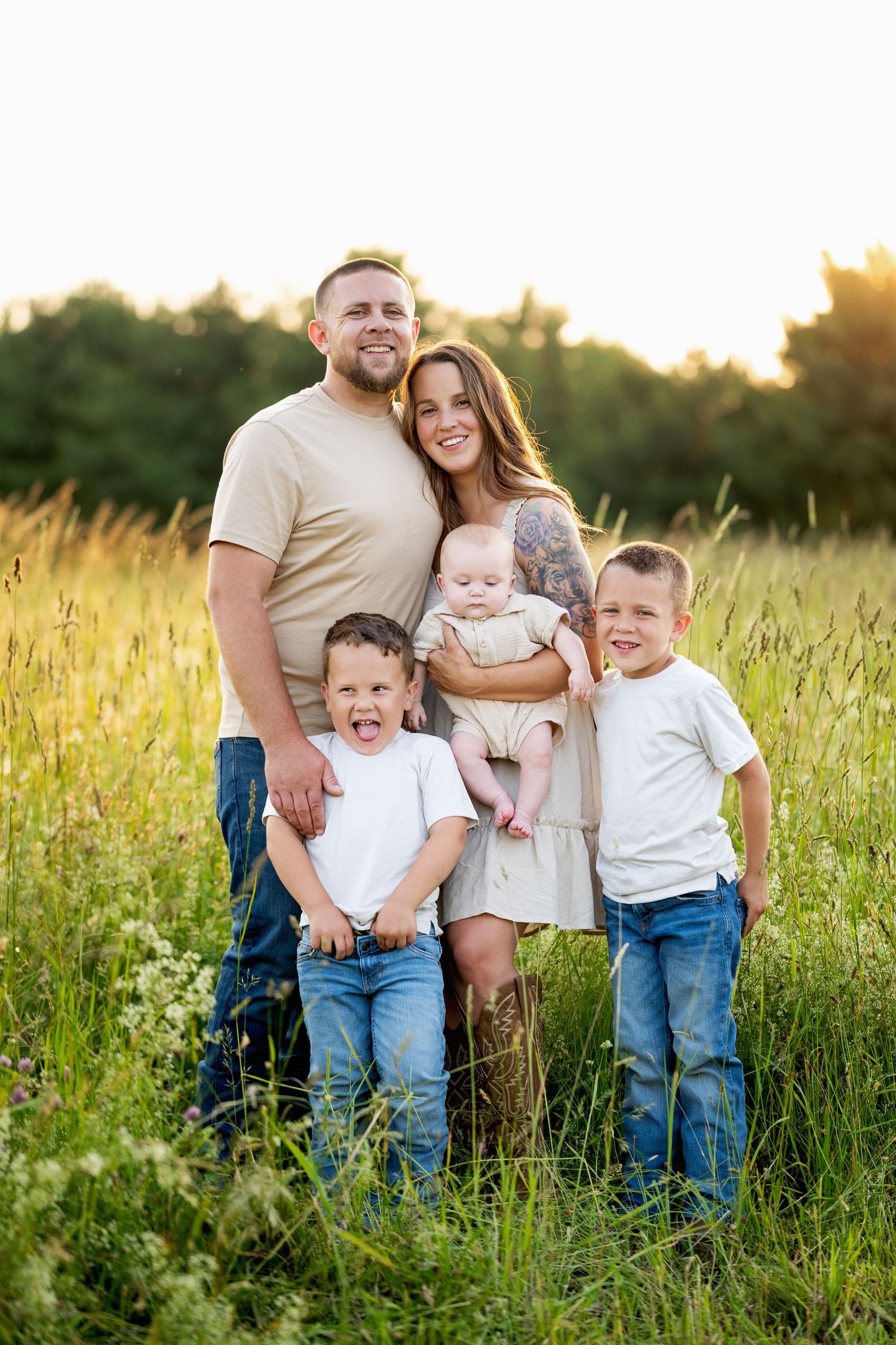 Family of five stands together in a tall grass field at sunset during a summer photo session.