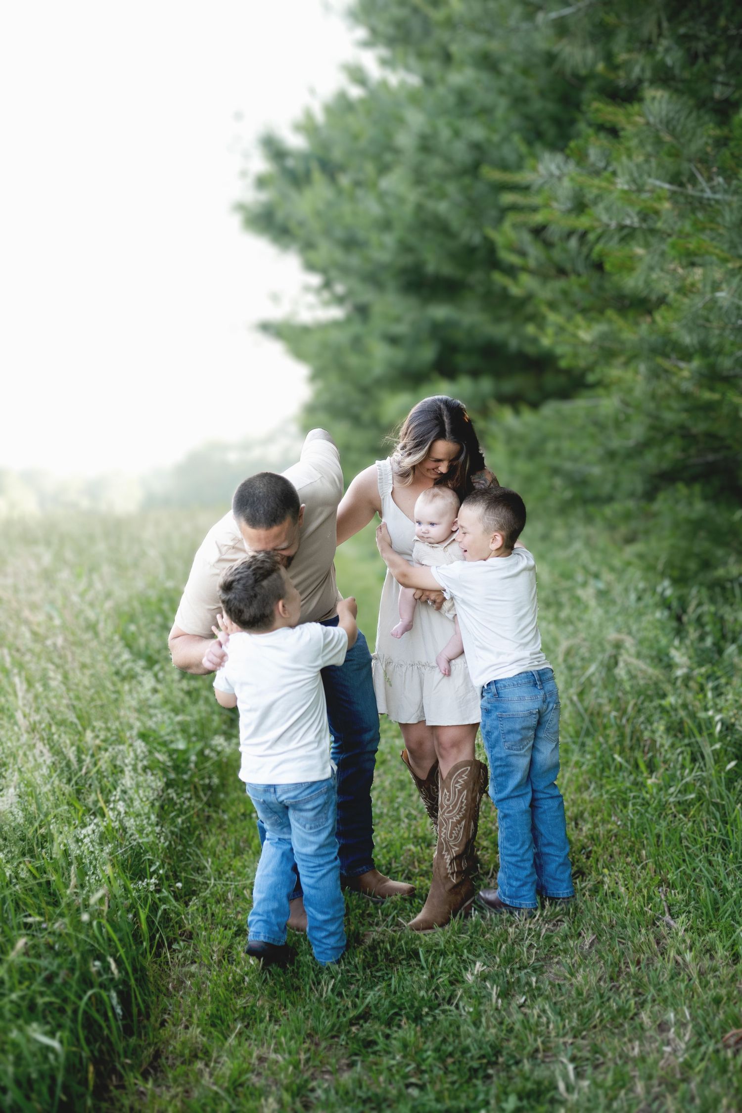 A heartwarming family moment together in a grassy meadow against evergreen trees on a misty summer day.