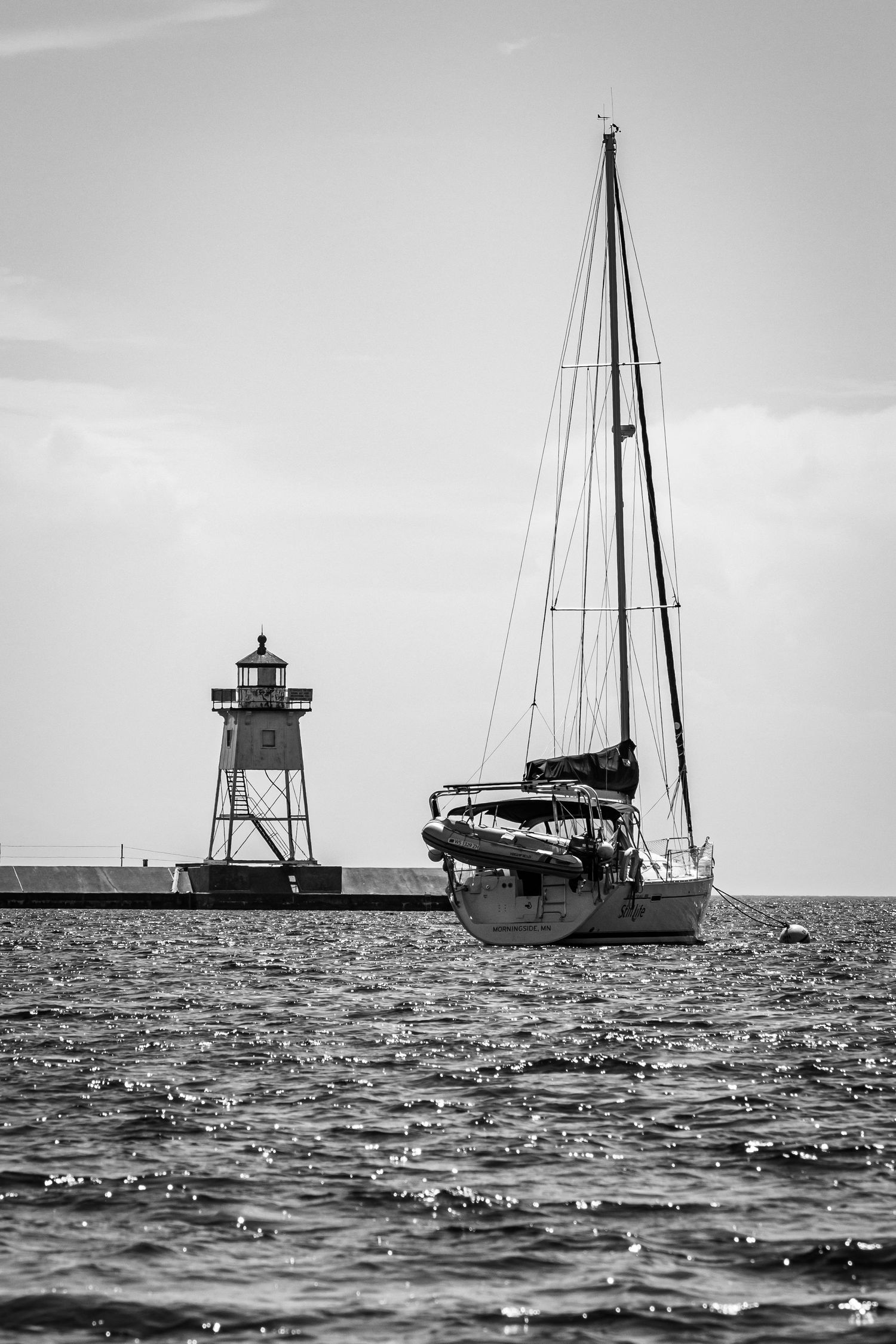 Photo of a sailboat and lighthouse in black and white.