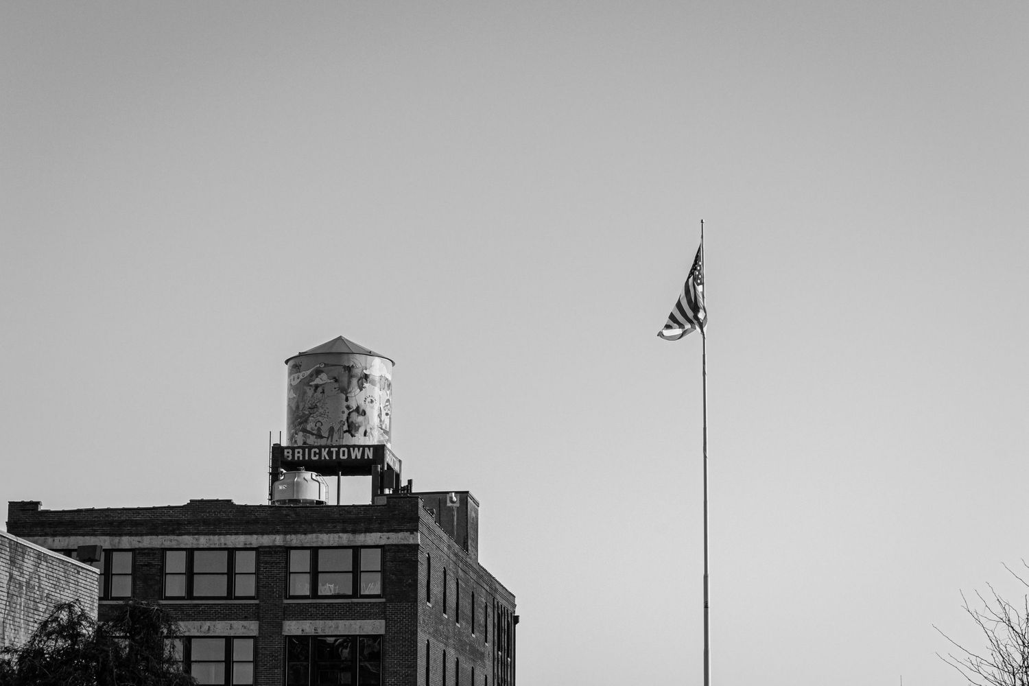Black and white photo of a watertower and the U.S. flag against the sky.