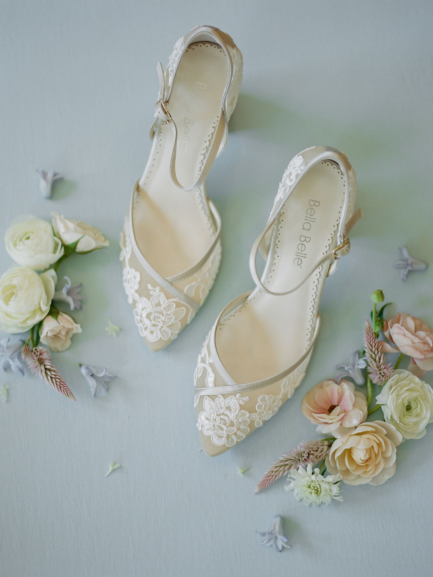 Elegant white lace bridal shoes displayed with blush and cream roses on a light gray surface at B.R. Cohn Winery in Sonoma.