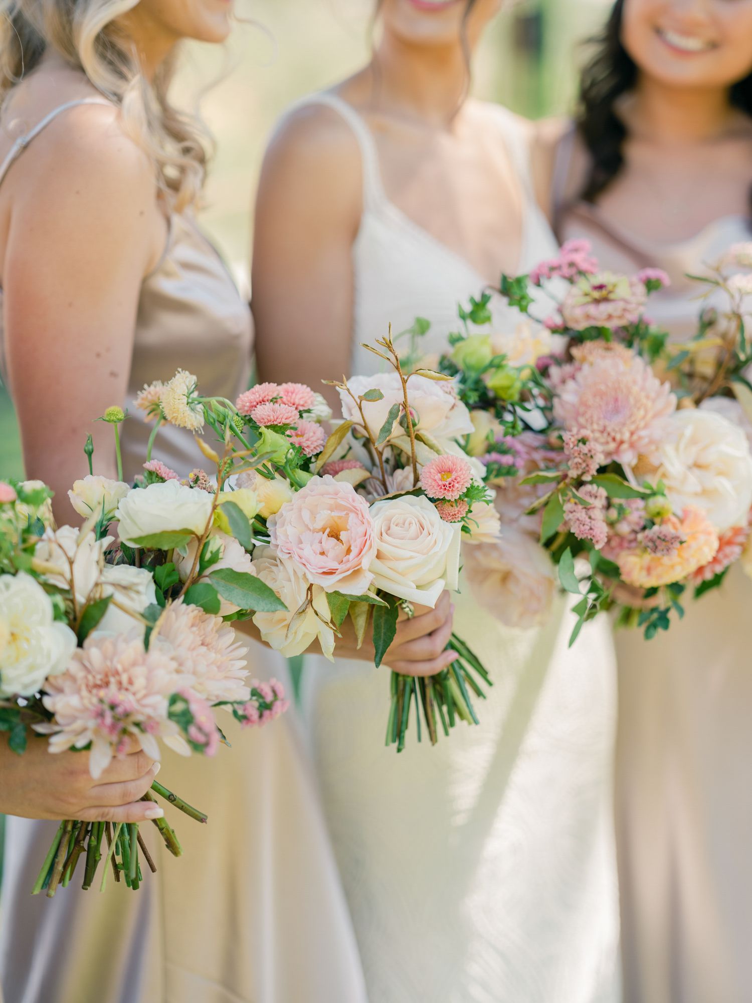 Three bridesmaids hold romantic blush and cream colored bouquets during an outdoor wedding in Napa.