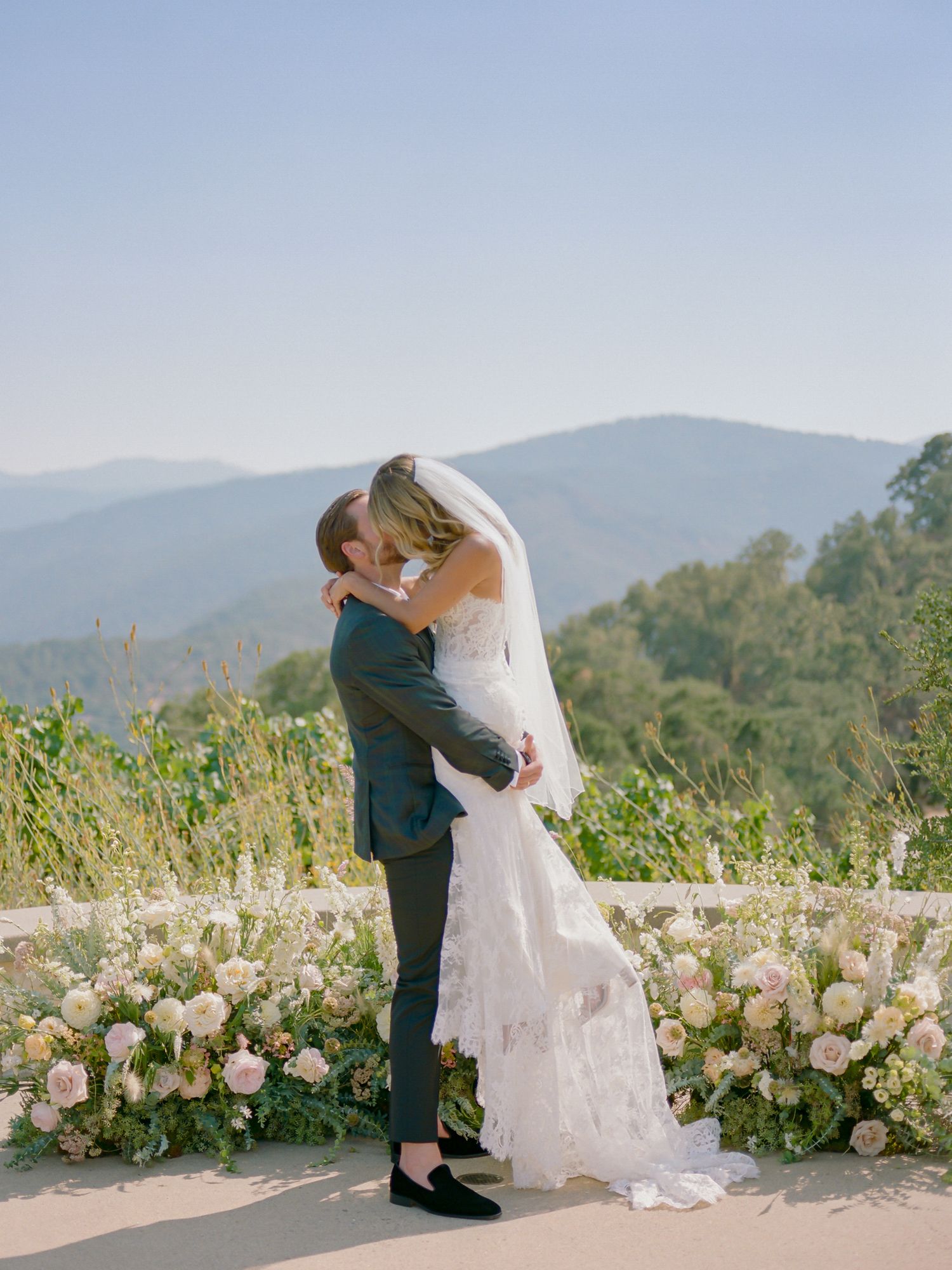 A romantic wedding moment captured against a mountain backdrop with pink floral decorations at Holman Ranch in Carmel Valley.