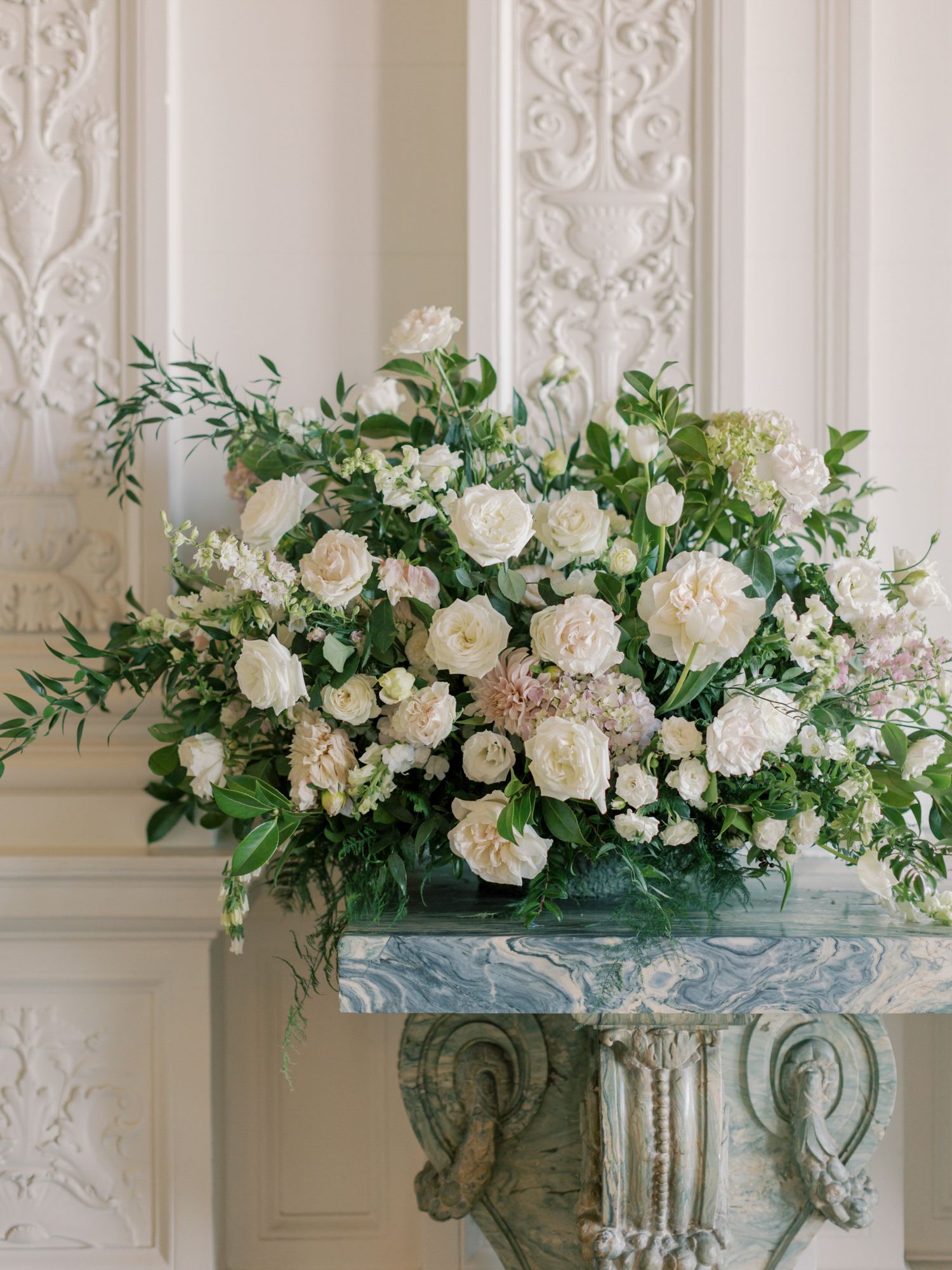 Ornate white floral arrangement with roses and greenery displayed against carved wall at Flood Mansion in San Francisco.