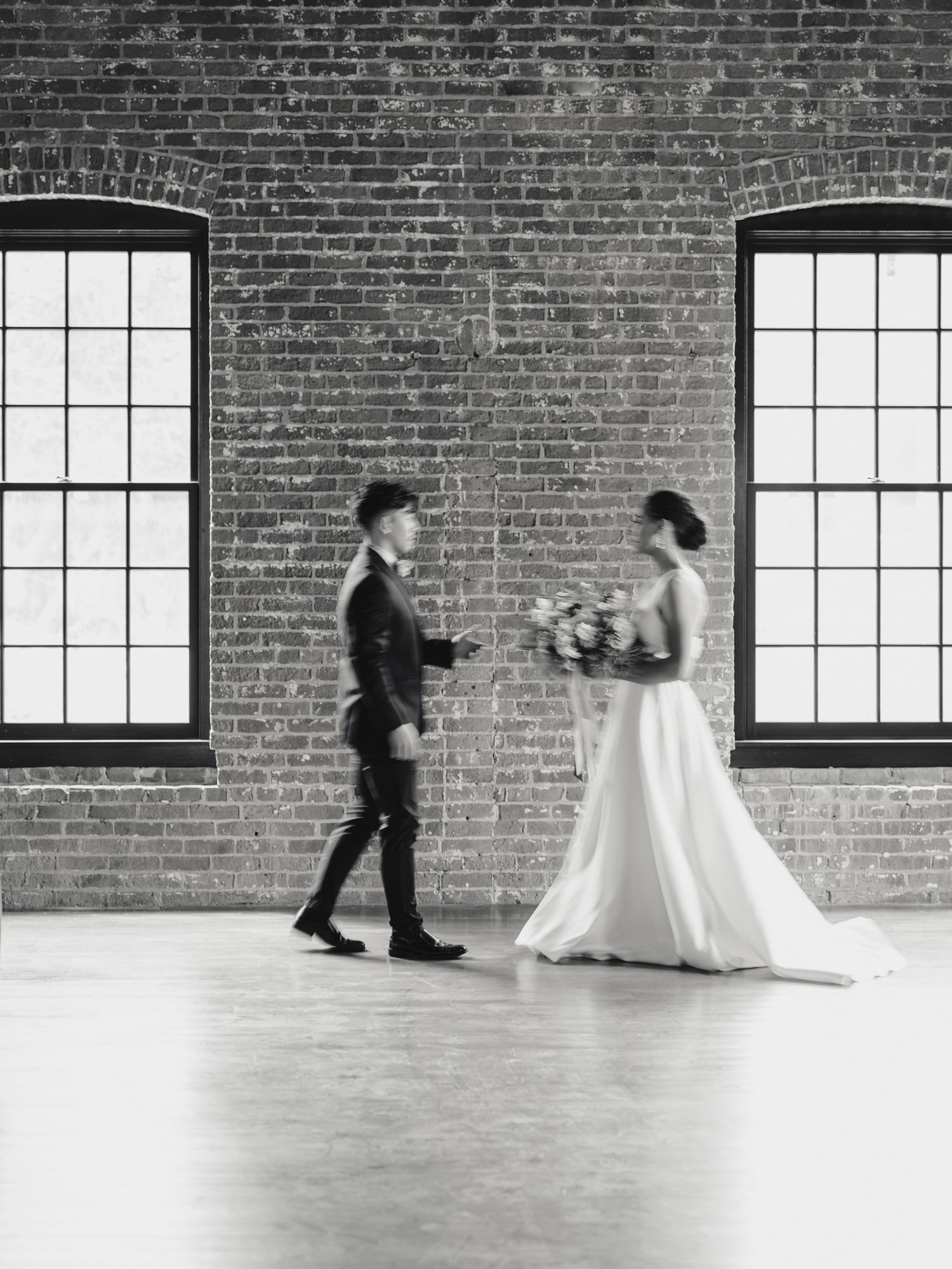 Black and white sequence of figures moving across empty room with brick wall and large windows in Napa.