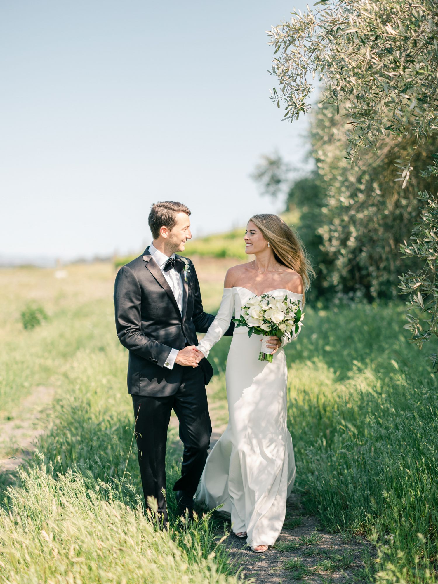 A romantic wedding photo of a couple walking together in a sunlit meadow with natural greenery background at Viansa Winery in Sonoma.