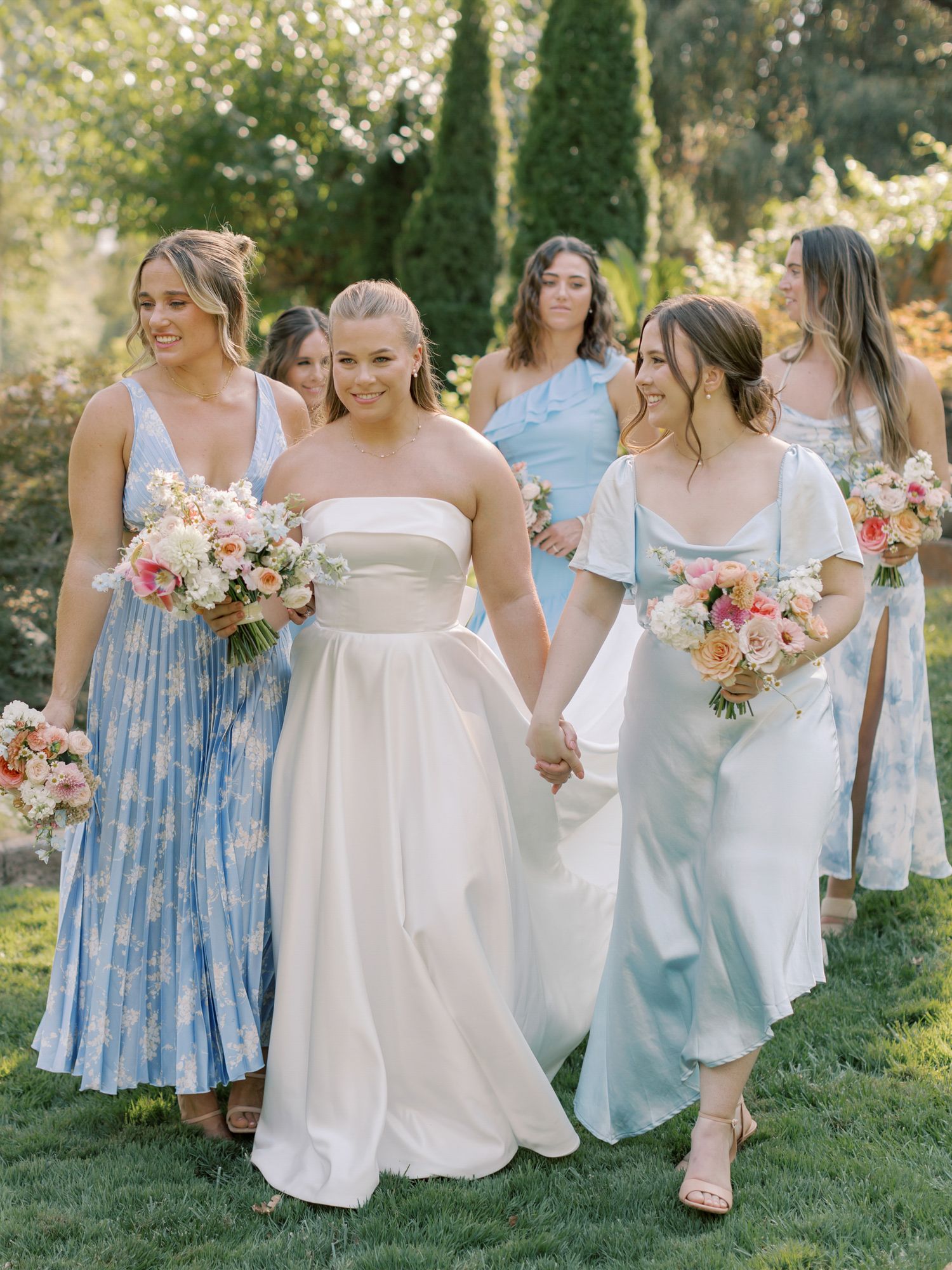 Wedding party in pastel dresses walking together through a garden setting in Napa.