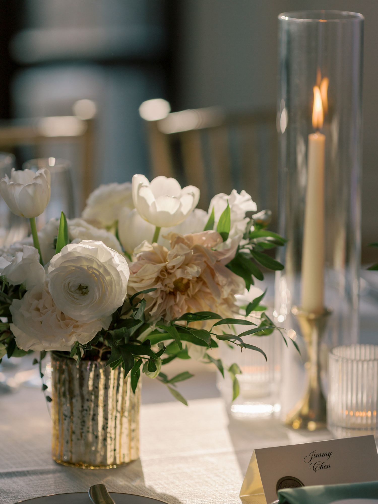 White ranunculus flowers in mercury glass vases alongside glowing candles on table setting at Flood Mansion in San Francisco.