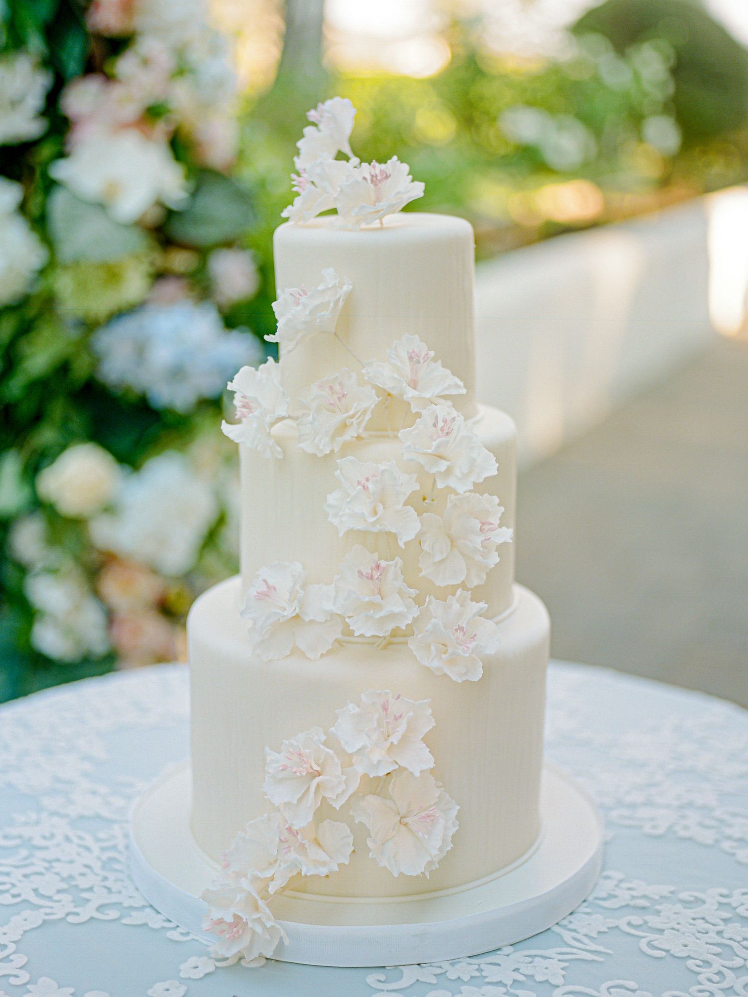 Elegant three-tier white wedding cake decorated with delicate sugar flowers at B.R. Cohn Winery in Sonoma.