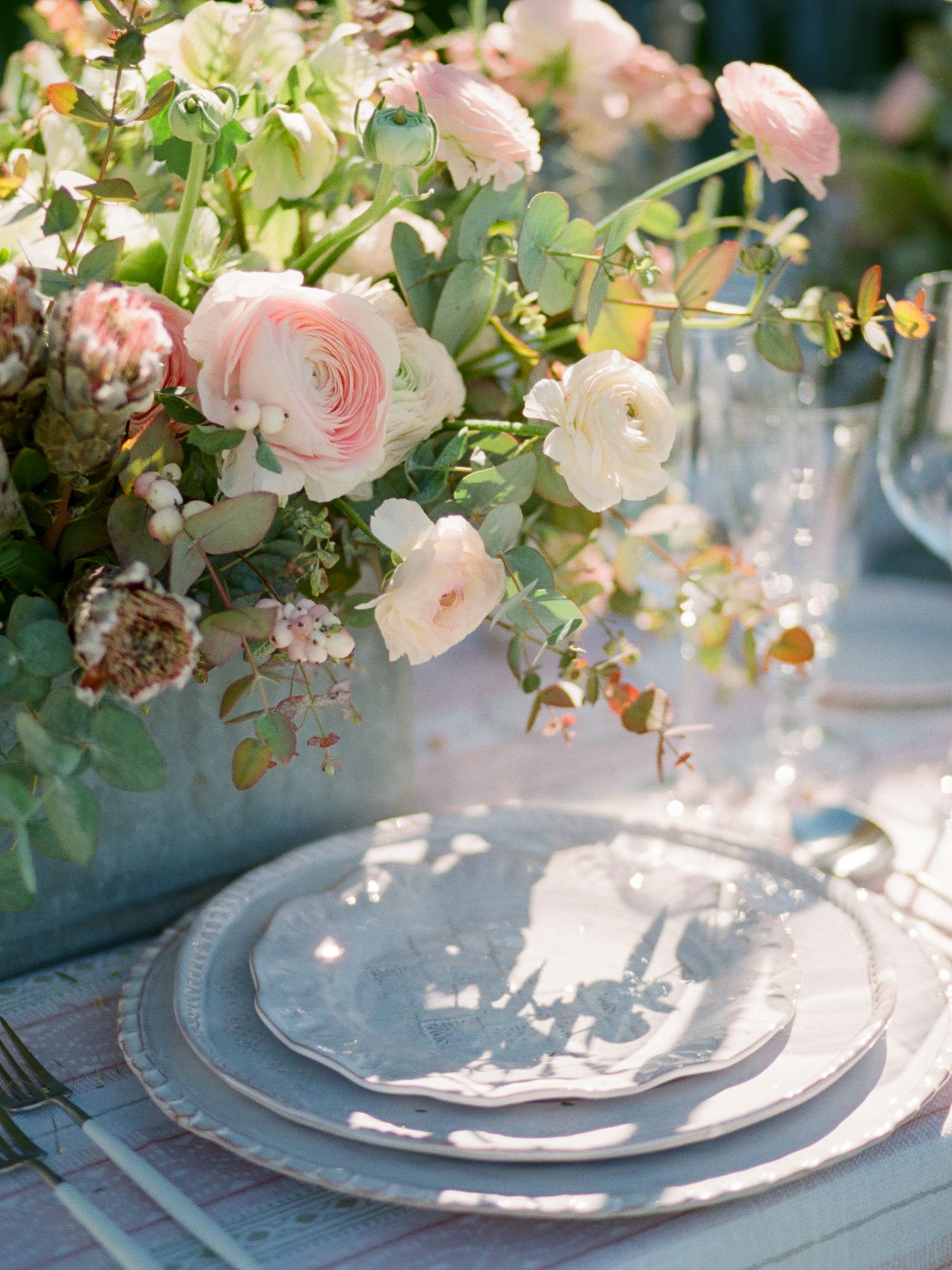 Elegant table setting with pink garden roses and eucalyptus centerpiece on blue tablecloth in Napa.