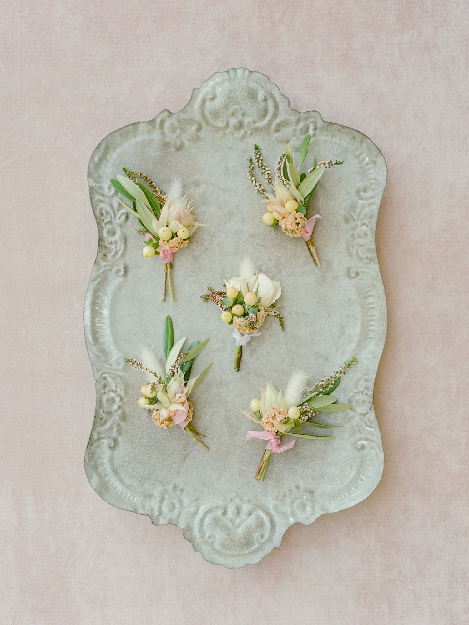 Five delicate floral boutonnieres arranged on an ornate vintage mint green platter in Napa.