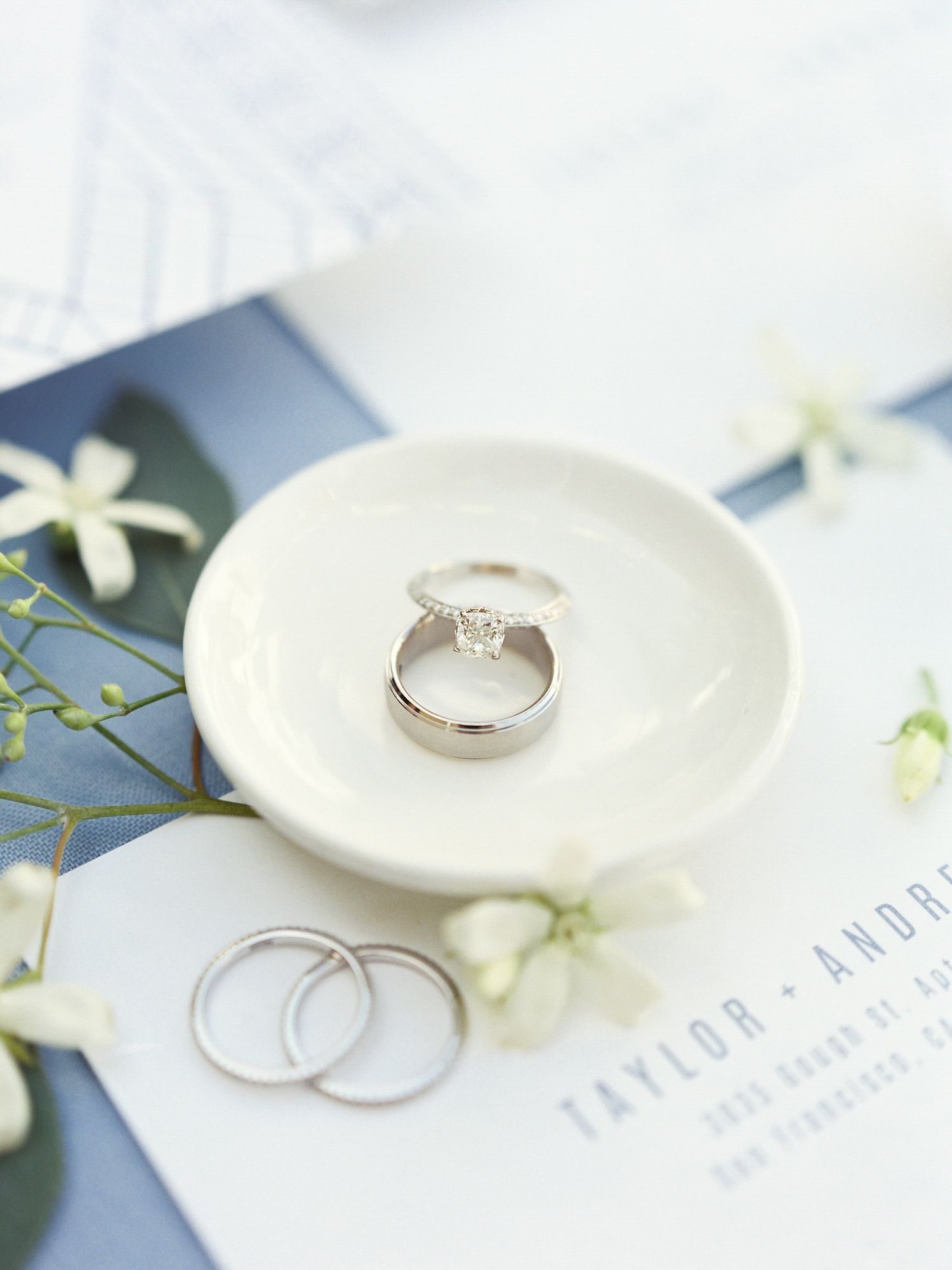 Wedding rings displayed on a white ceramic dish with delicate flowers and invitation details at Vine Hill House in Sebastopol.