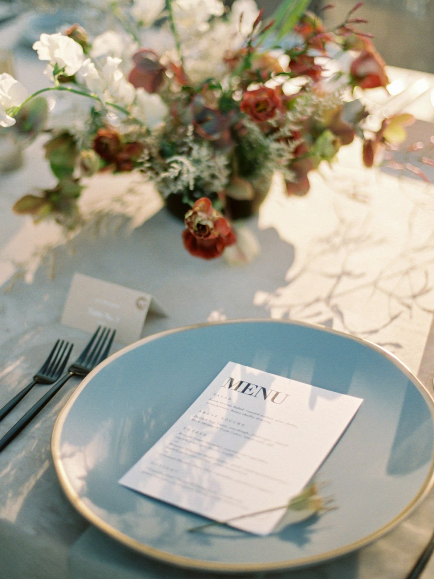 Elegant place setting with menu card and floral centerpiece on light blue plate with gold rim at Park Winters.