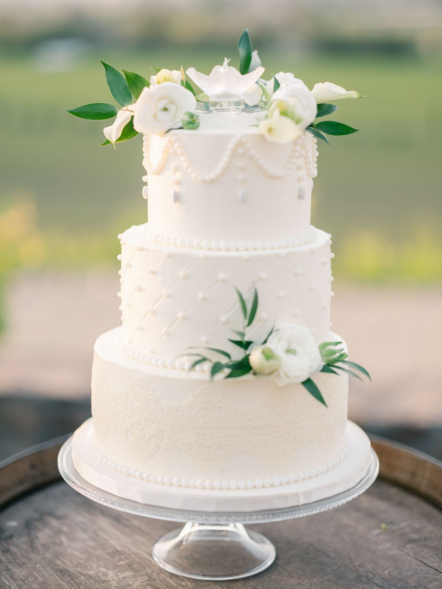 Classic three-tier white wedding cake decorated with fresh white flowers and greenery at Viansa Winery in Sonoma.