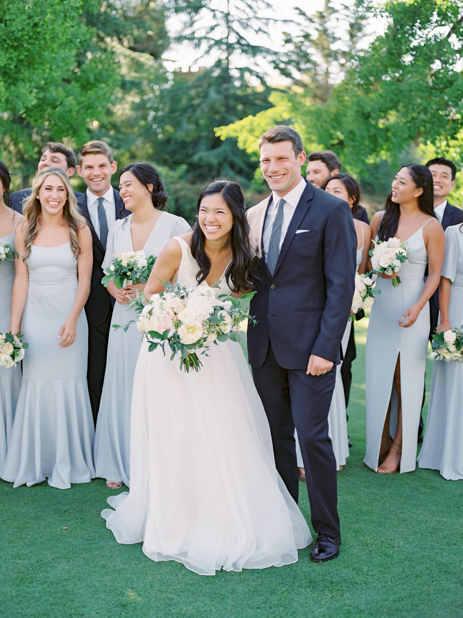 Wedding party in light blue bridesmaid dresses and navy suits posing on green lawn at Claremont Country Club in Oakland.