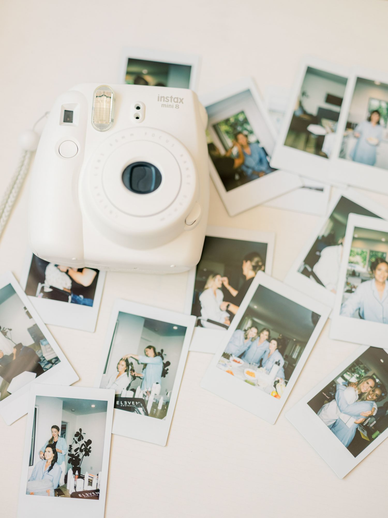 White Instax instant camera surrounded by scattered polaroid photos on white surface at The Barn at Harrow Cellars in Sonoma.