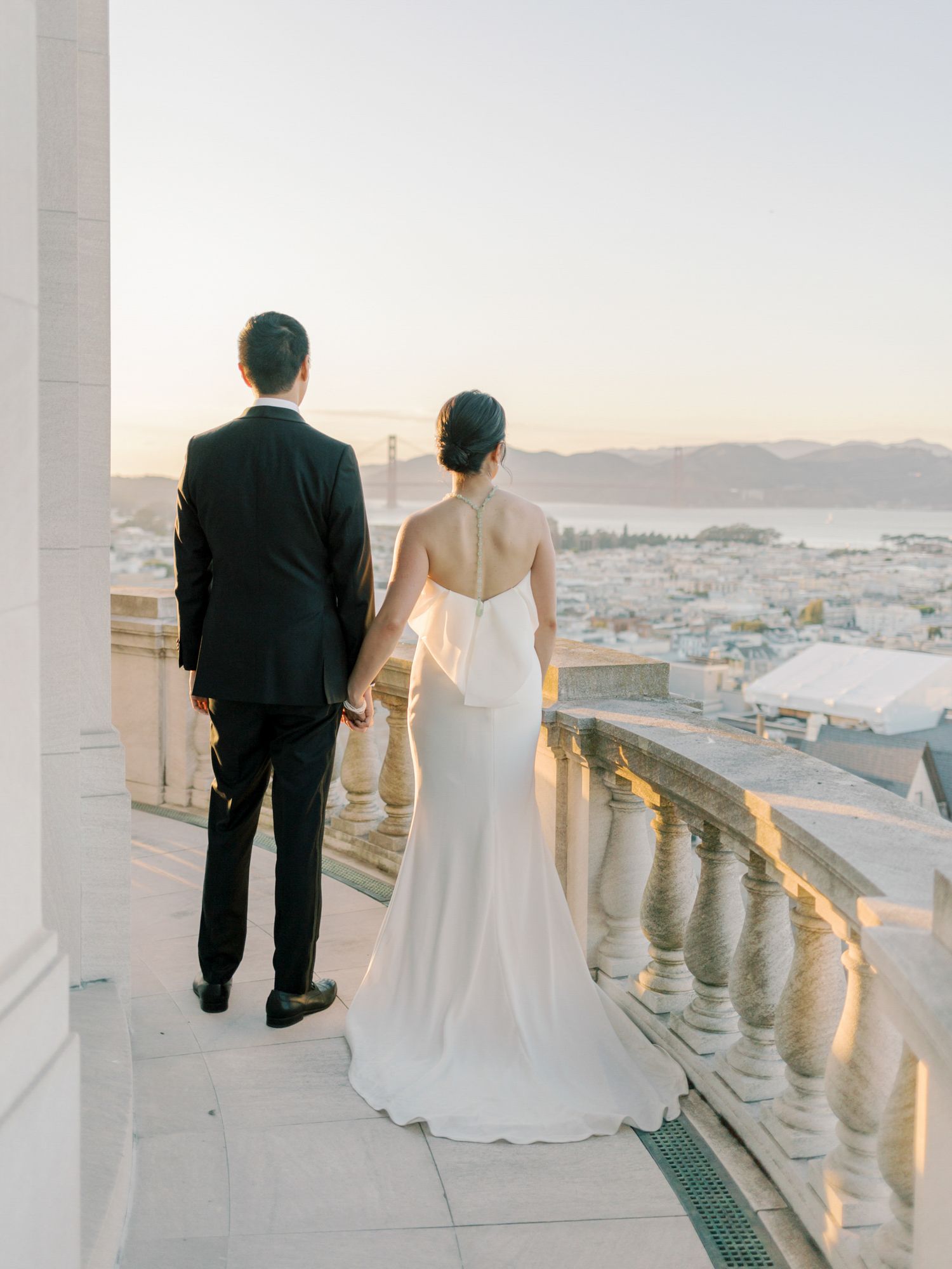 Newlyweds overlooking San Francisco and the Golden Gate Bridge at sunset from a balcony at Flood Mansion.