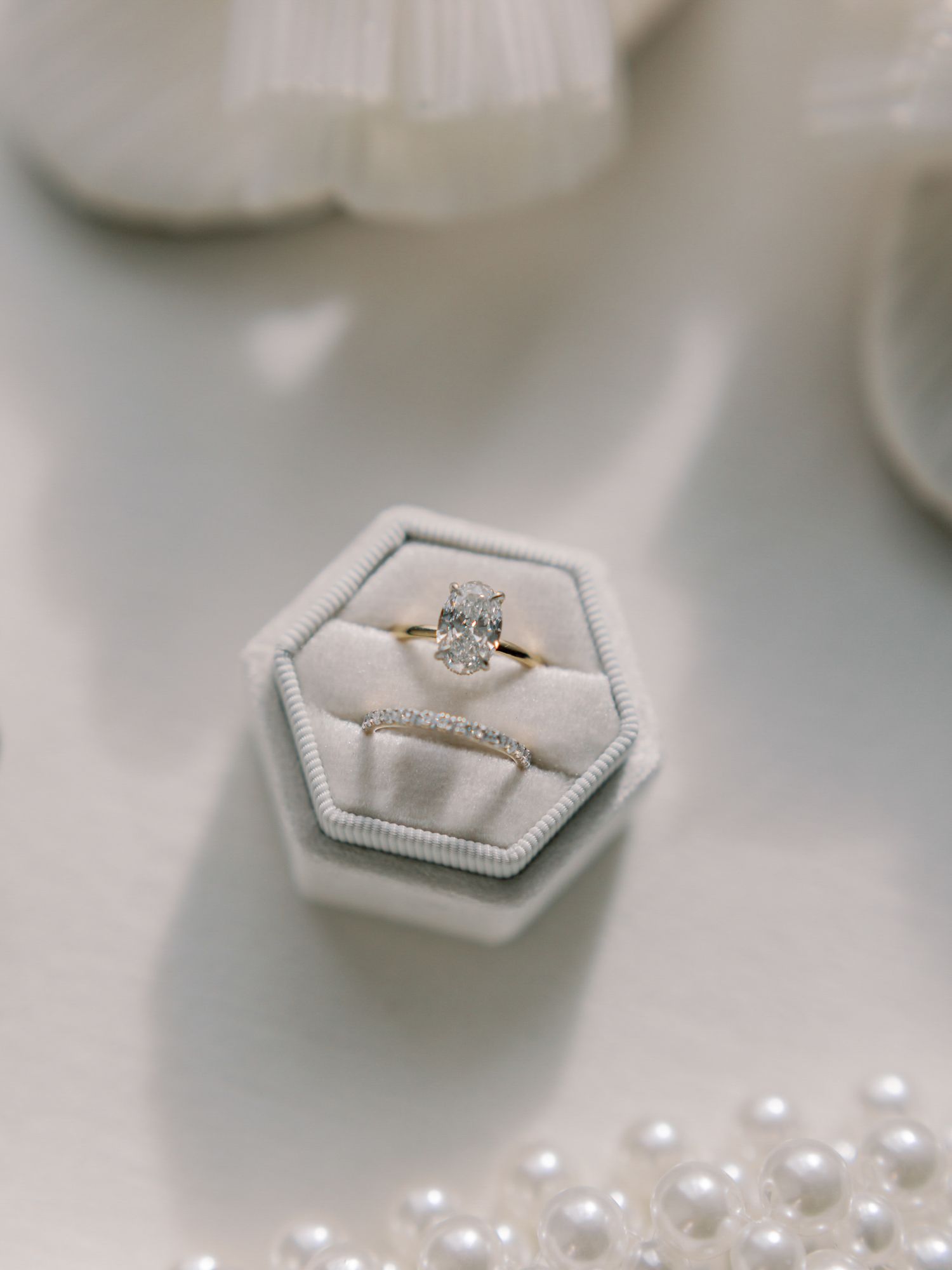 Wedding rings displayed in white hexagonal boxes with scattered pearls on light surface at Greystone in St. Helena.