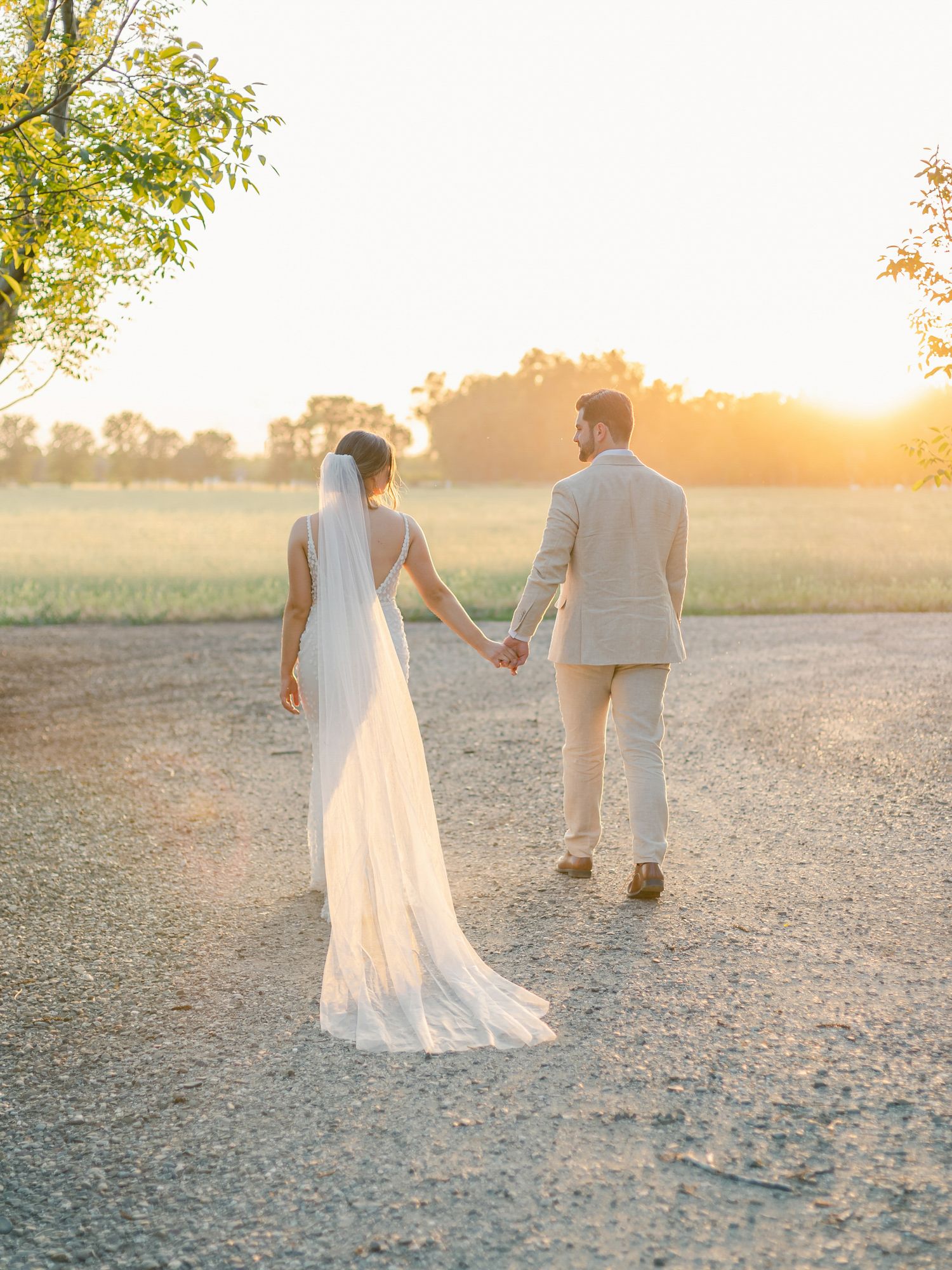 A couple walking hand in hand at sunset on a dusty country road during their wedding at The Barn at Pheasant Trail Ranch in Chico.