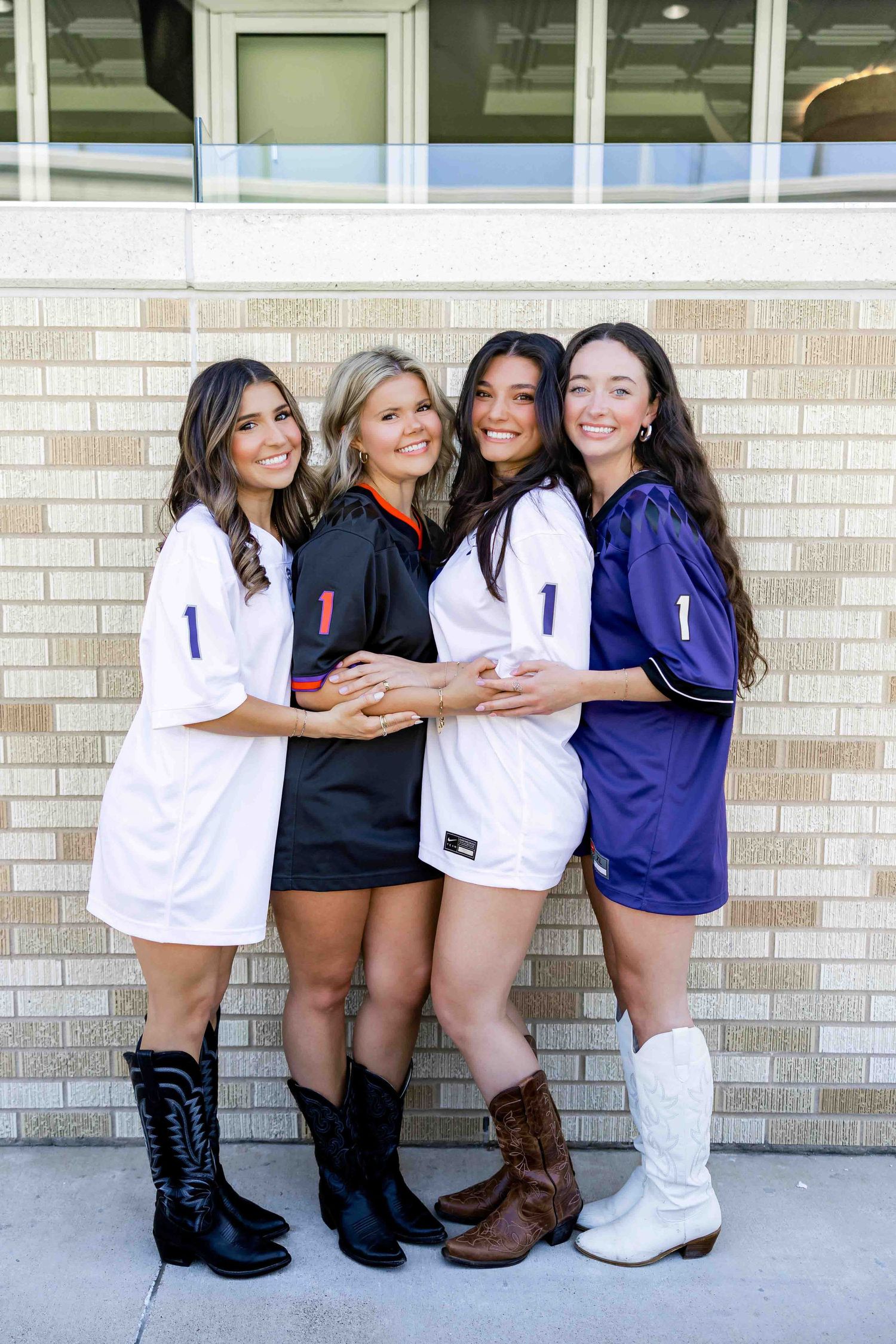 Friends in sports jerseys and boots posing together against brick wall.
TCU Graduation photographer