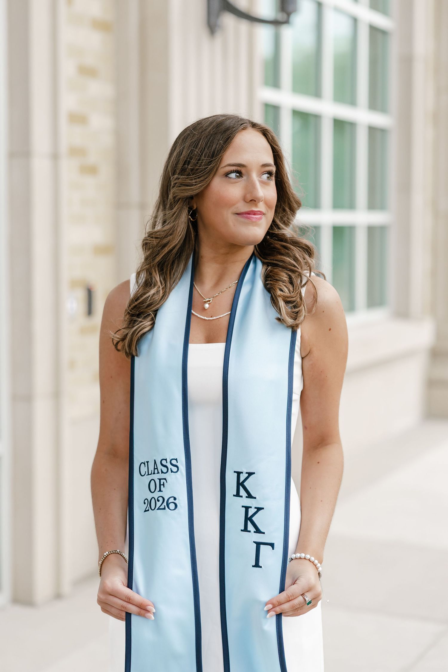 Young woman wearing a light blue Kappa Kappa Gamma graduation stole reading Class of 2026, posing outdoors.