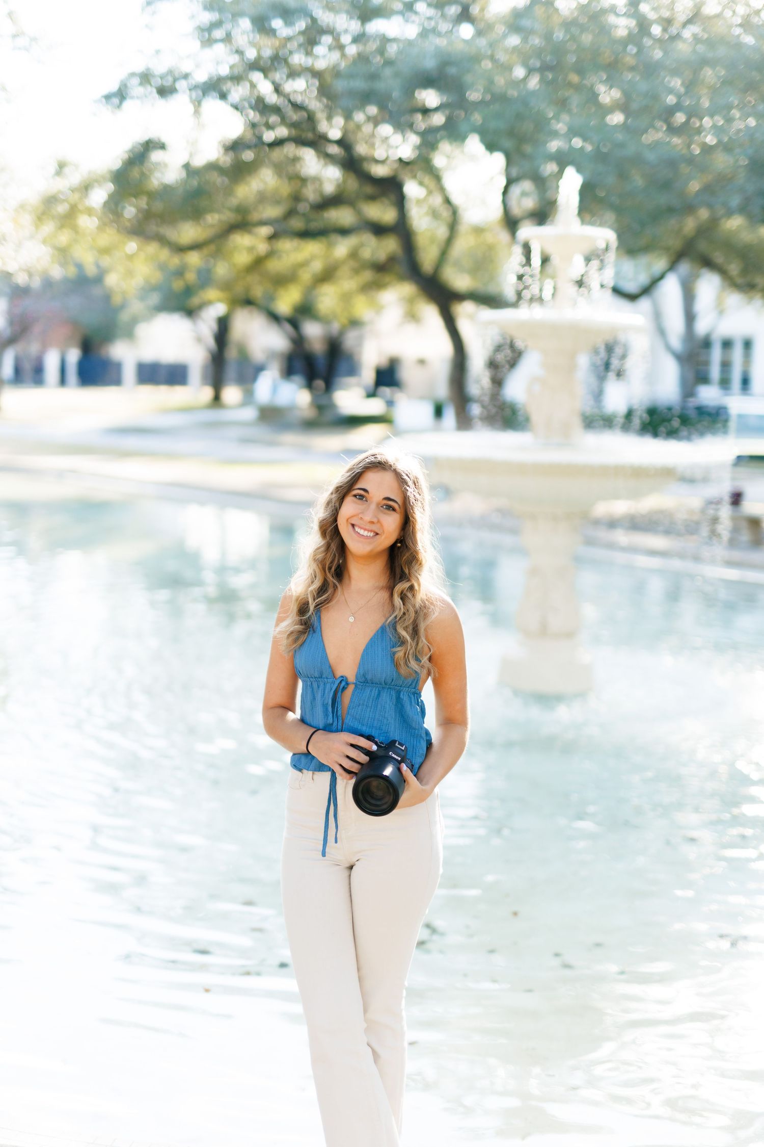 Portrait of photographer by fountain holding camera in casual outfit.
