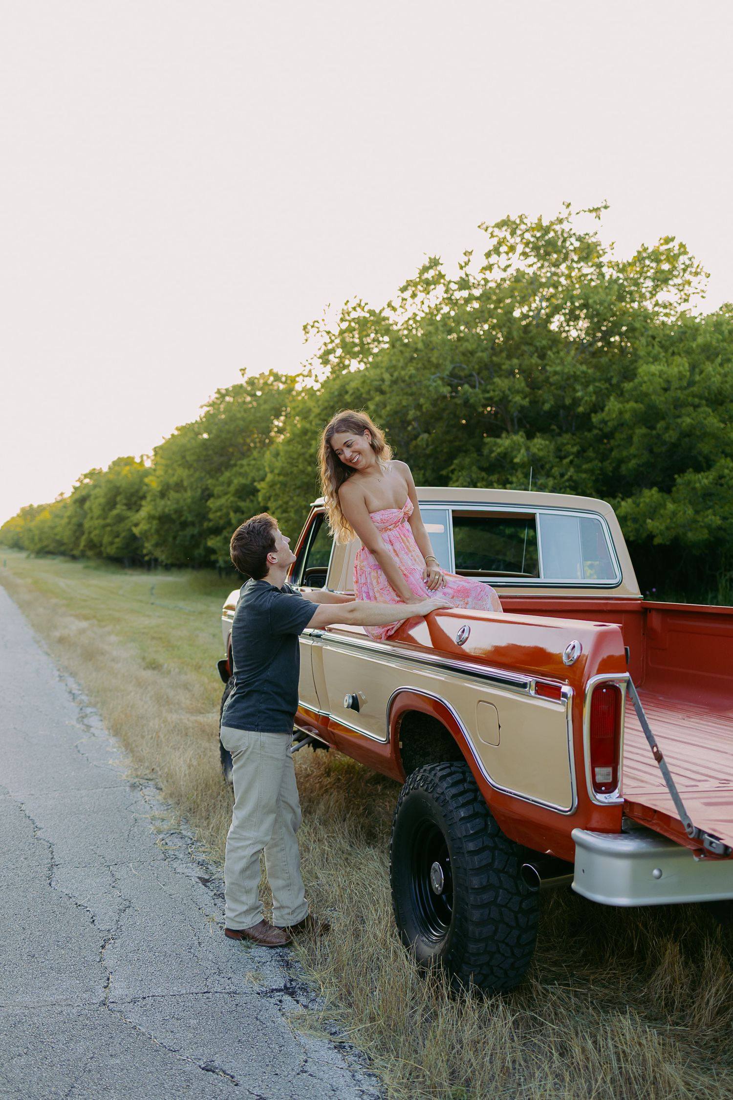 A sequence of four images showing people interacting with a vintage red and beige pickup truck on a rural road at sunset.