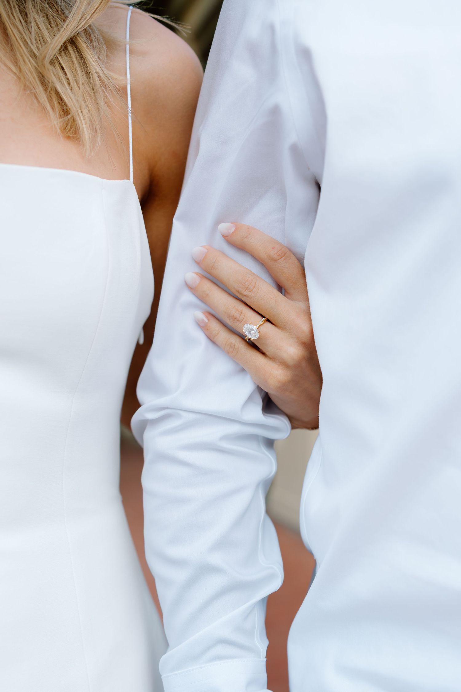 Close-up view of couple embracing in white attire with gold wedding band visible on hand.