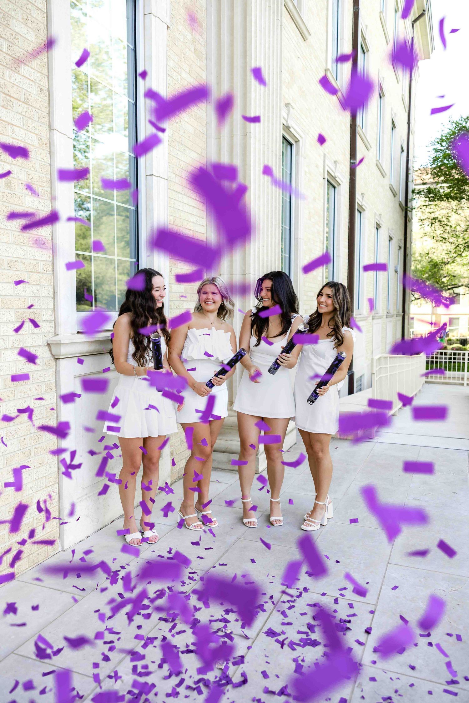 A group celebrating with purple confetti in white dresses outside a building.
TCU Graduation photographer